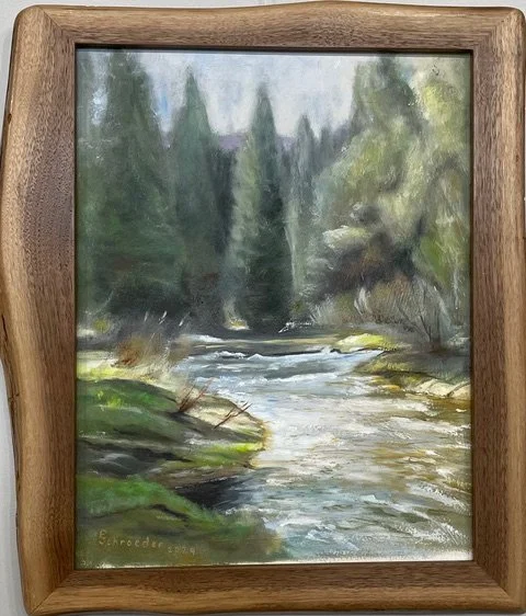 A watercolor painting of a river flowing through a forest with tall trees and greenery on both sides, framed in a wooden frame.