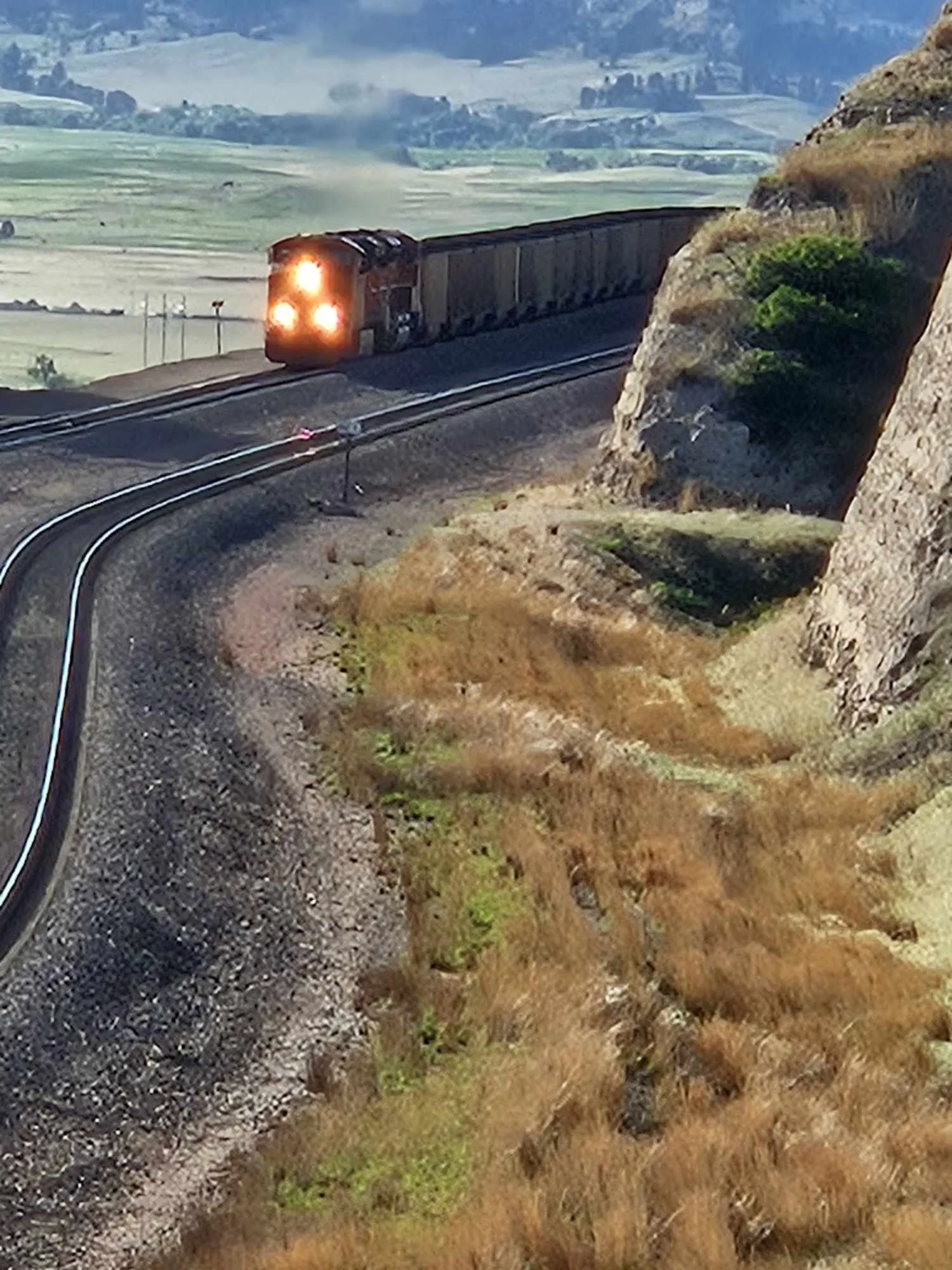 A train traveling around a curved track in a hilly landscape with grassy fields and rocky hillsides.