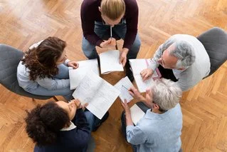 Five people gathered around a table with documents and a laptop, having a business meeting.