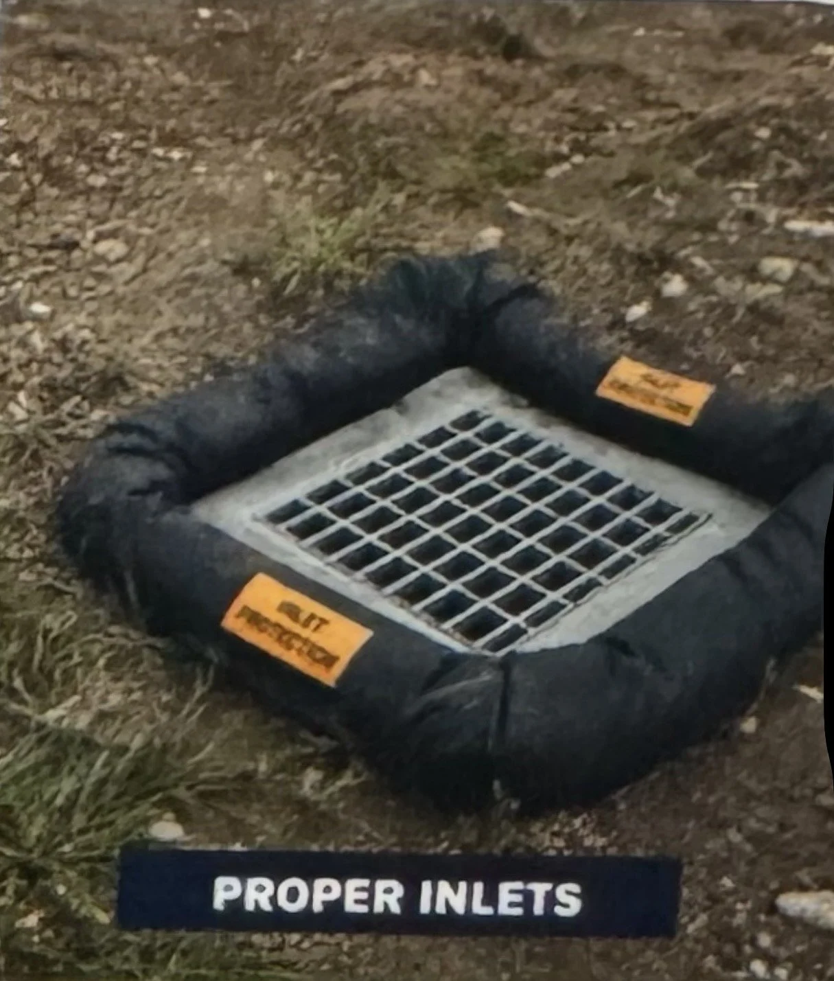 A black inflatable boat with proper inlets sticker, resting on a dirt and grass surface.