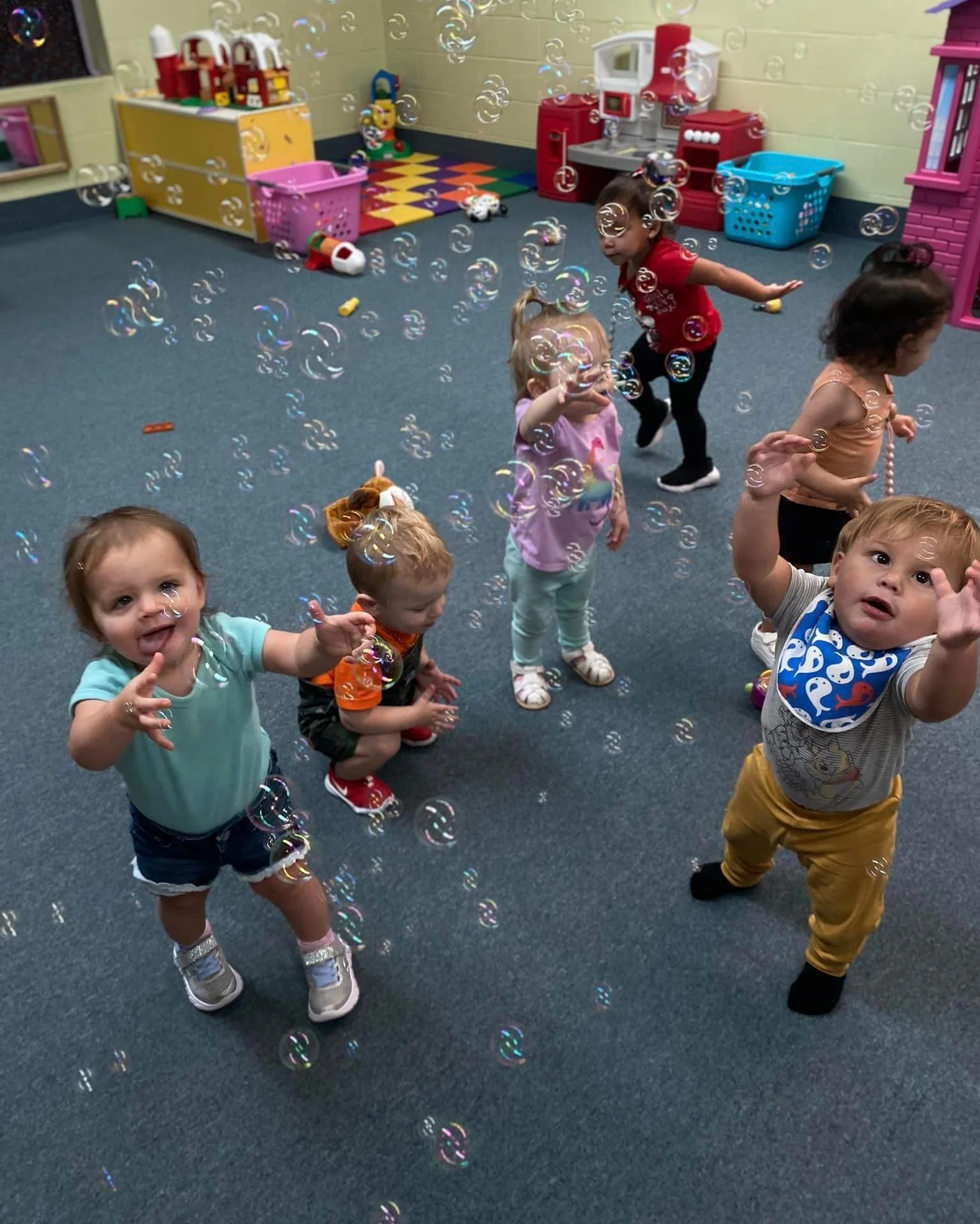 Children playing with bubbles in a playroom with toys and colorful furniture.