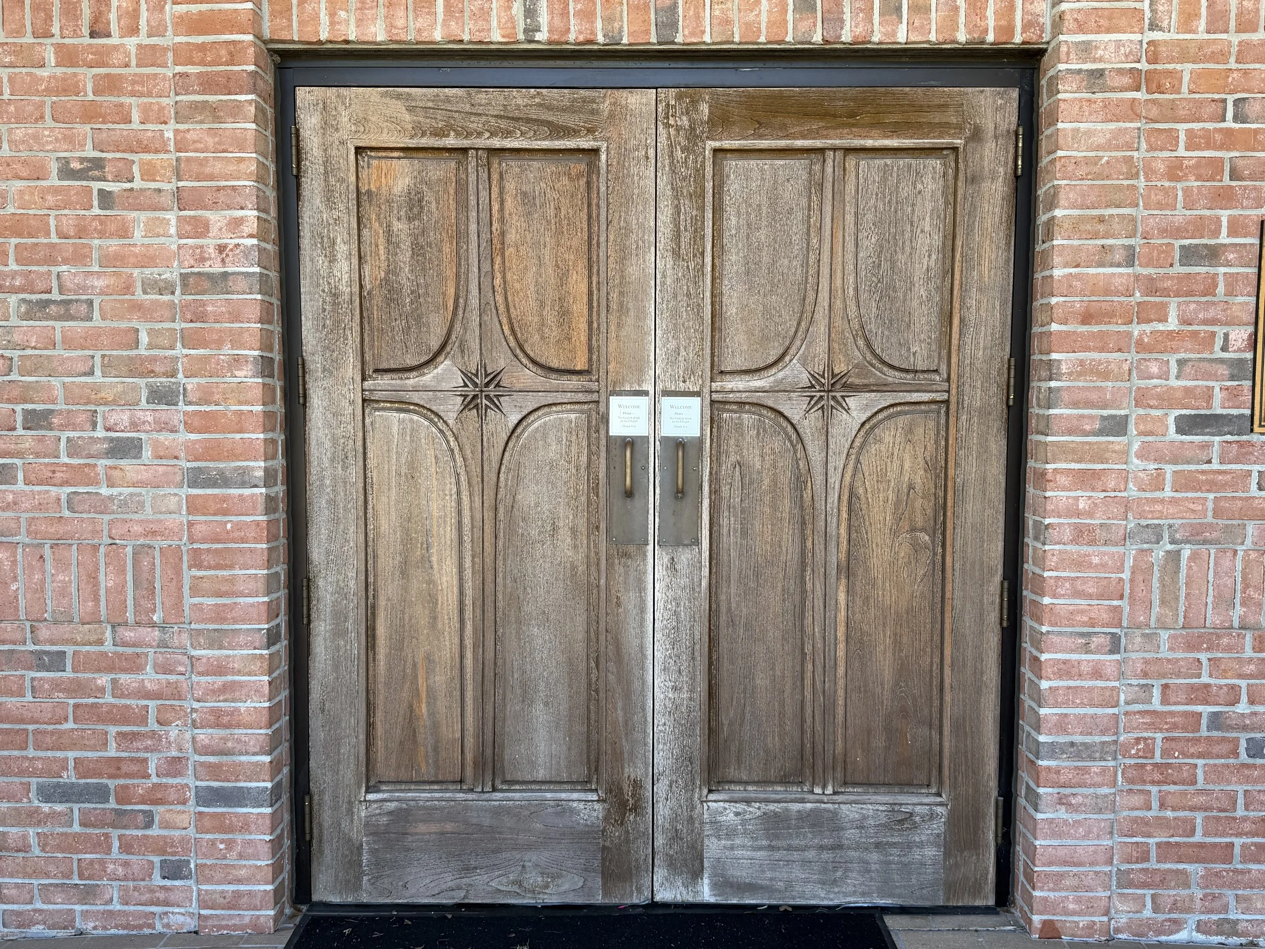 Double wooden doors with decorative engraved patterns, set within a brick wall.