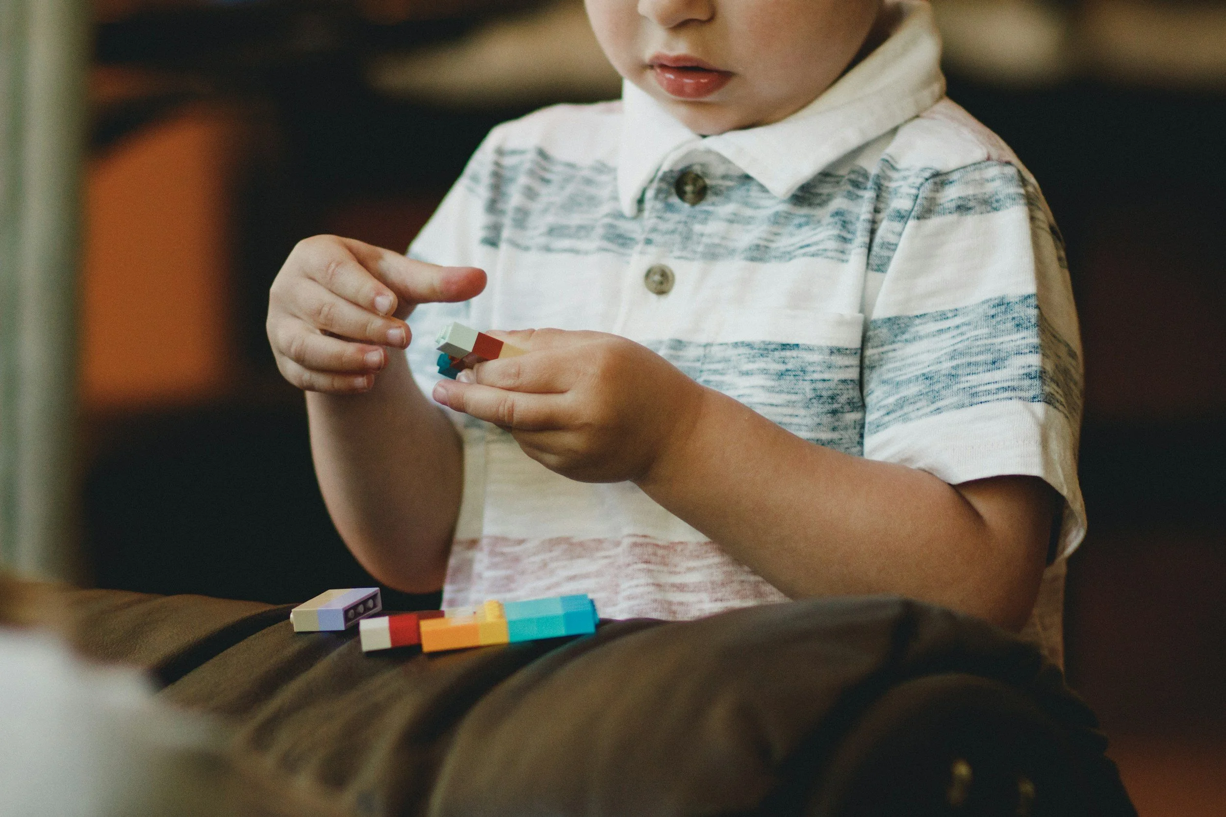 A young boy wearing a striped polo shirt sitting and playing with colorful building blocks.