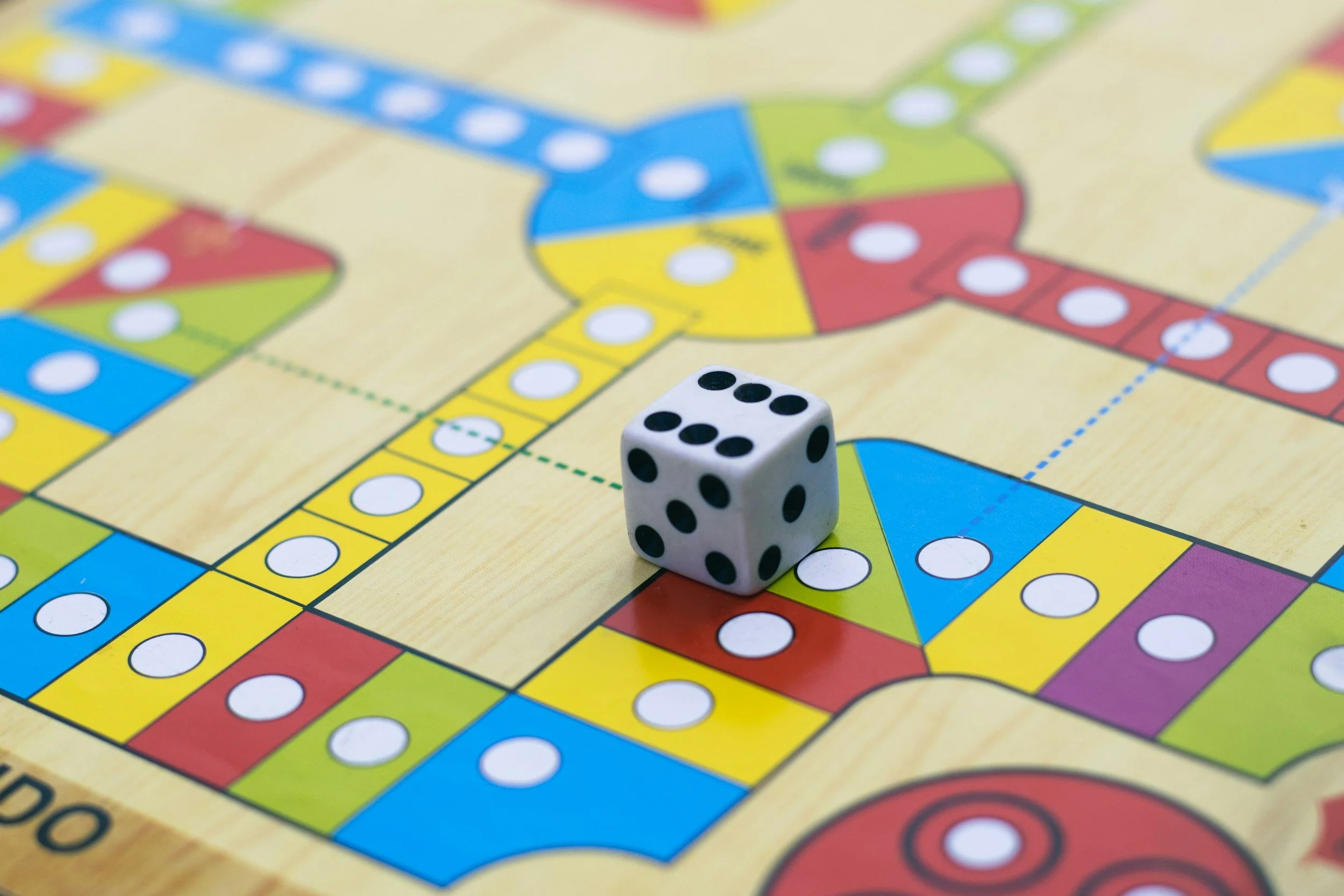 Close-up of a white six-sided die showing the number five placed on a colorful Monopoly game board.