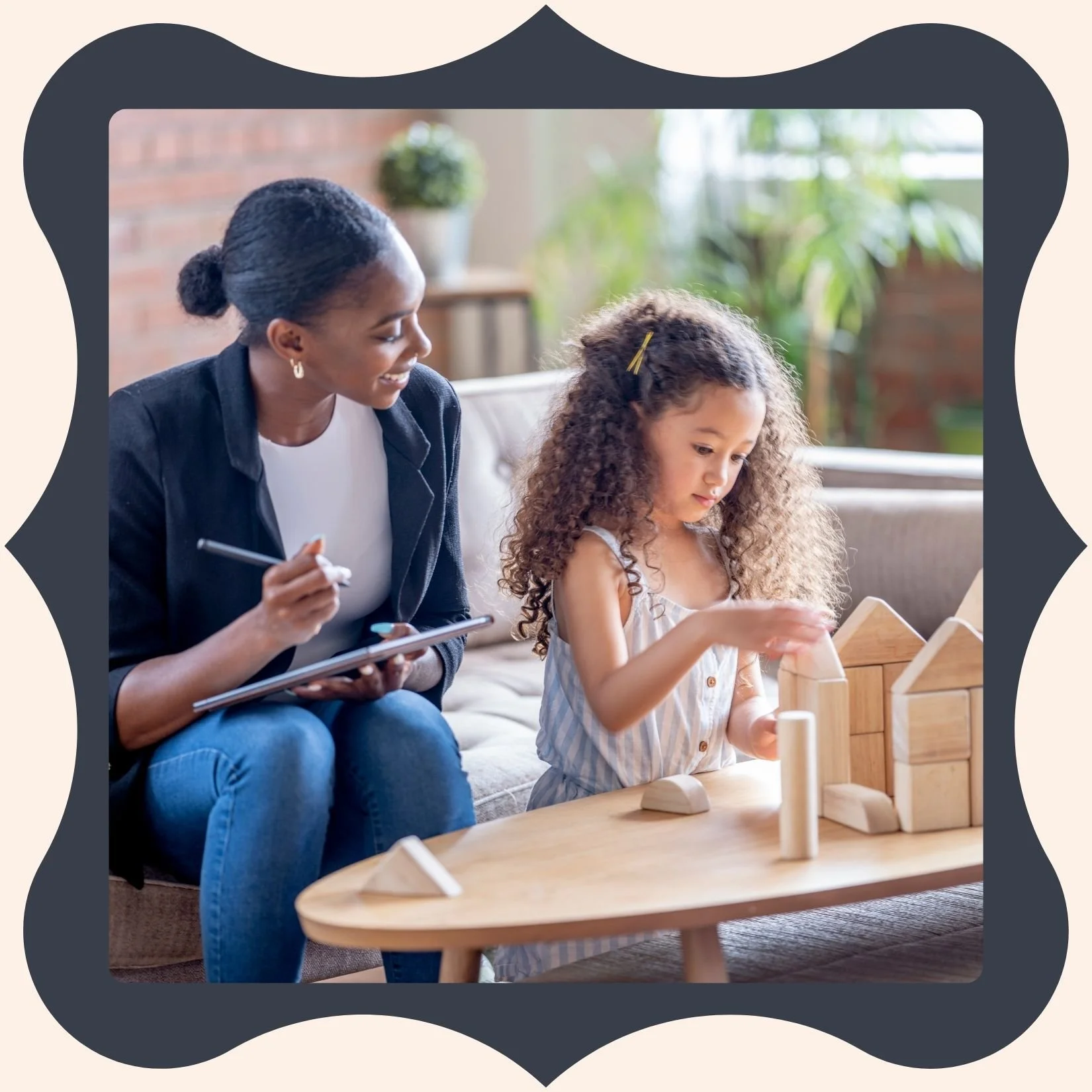 A woman and young girl sit on a sofa, playing with wooden building blocks on a table. The woman is smiling and holding a tablet with a stylus, while the girl is focused on stacking blocks. The setting appears cozy with indoor plants and a brick wall in the background.