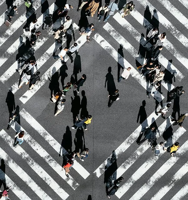People crossing a busy intersection in various directions on a crosswalk.