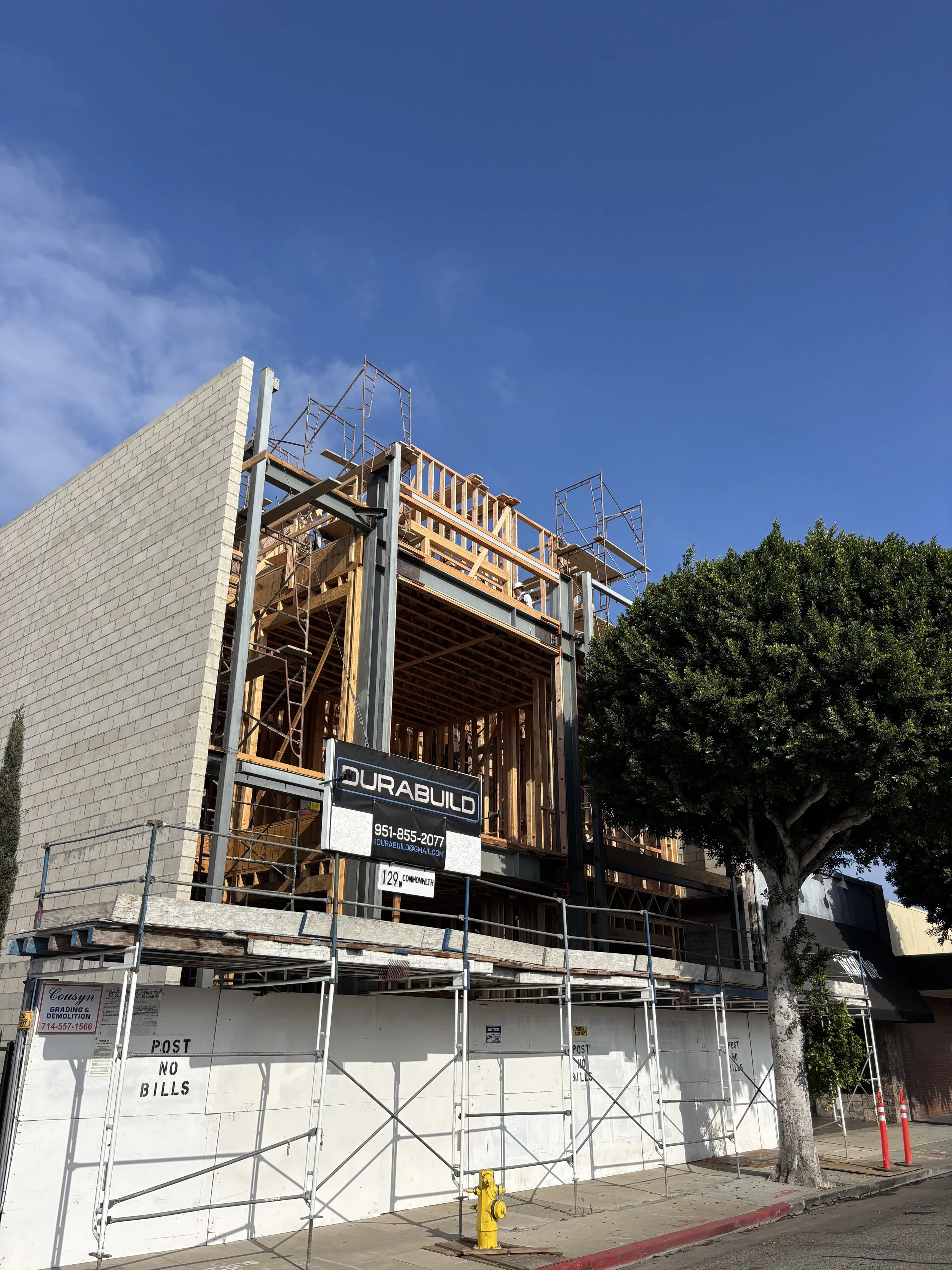 Construction site of a building with scaffolding, wooden framework, and a partially completed brick wall on a sunny day with clear blue sky.