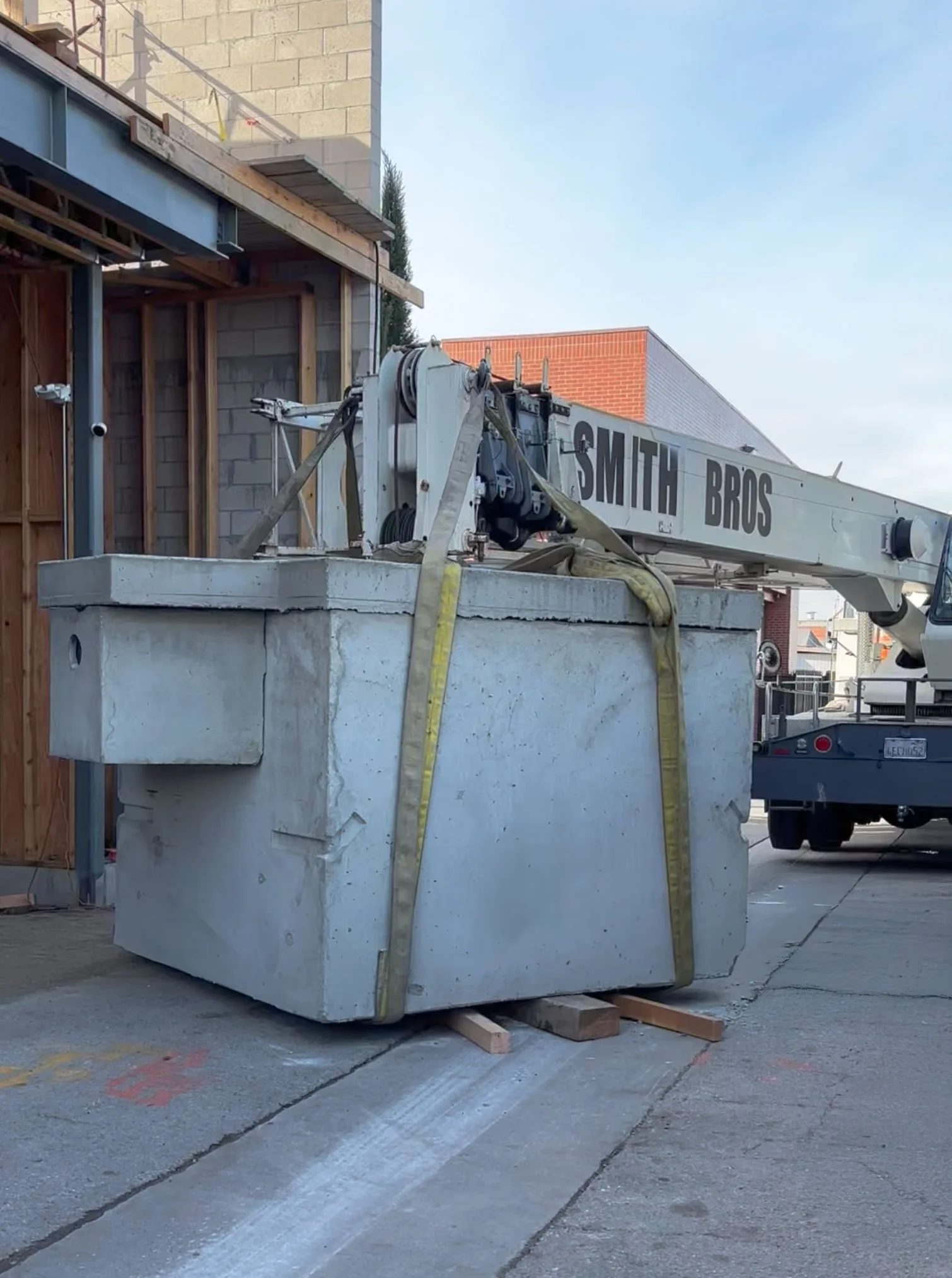 A construction crane with the words 'SMITH BROS' on its arm, parked on a sidewalk next to a partially constructed building.