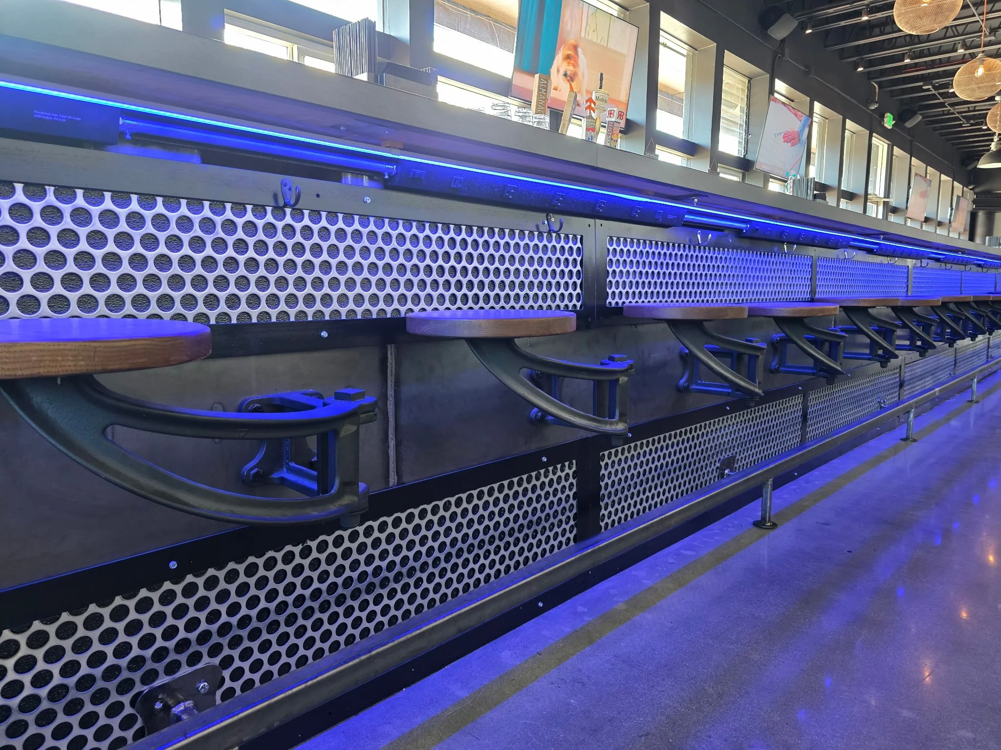 Empty barstools lined up along a counter with blue lighting, in a modern bar or restaurant.