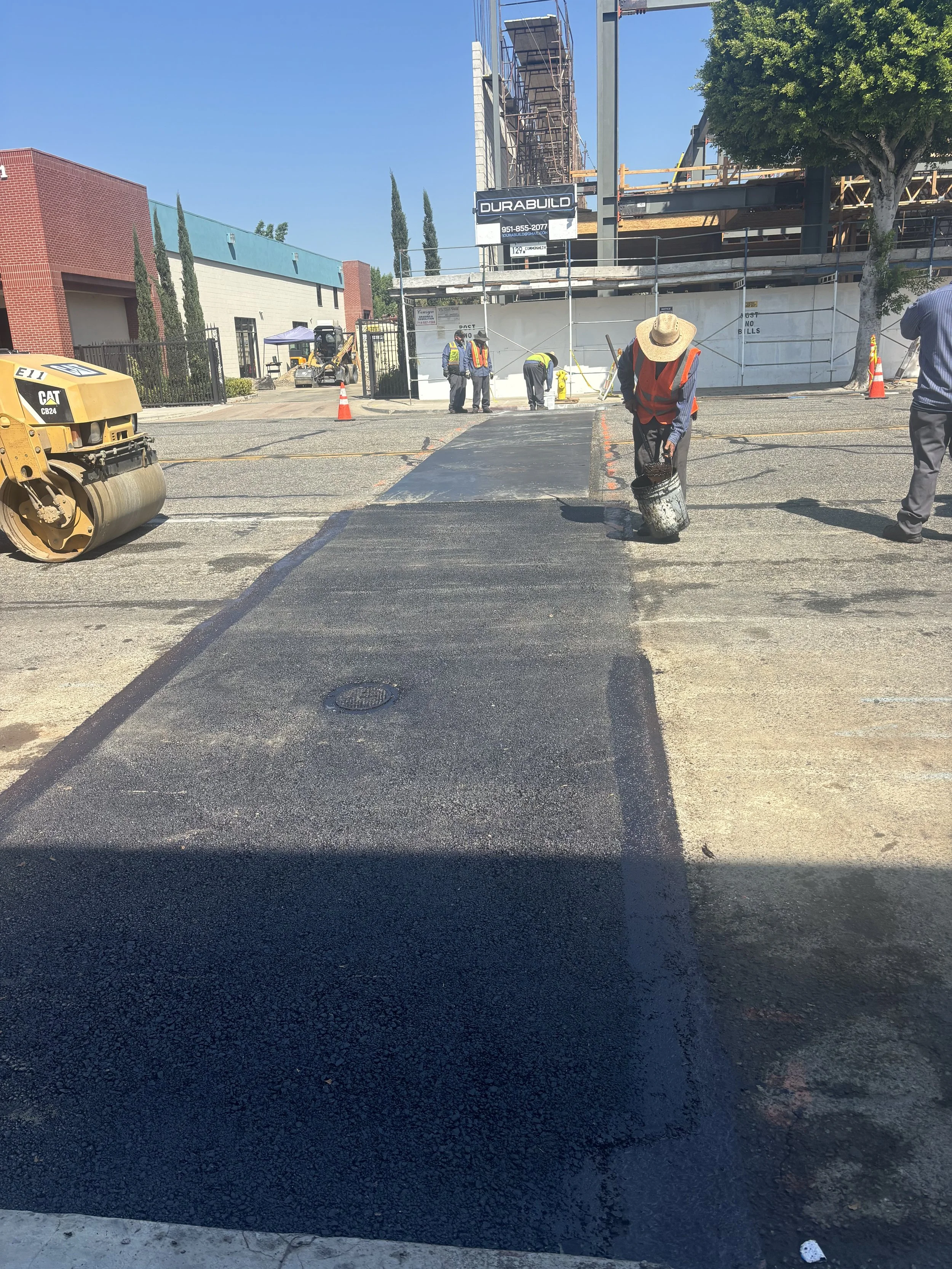 Construction workers paving a street, with equipment and scaffolding in the background.