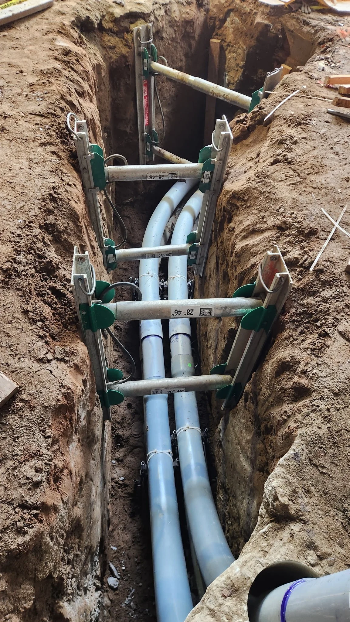 Underground construction site with PVC pipes and metal supports in a trench.