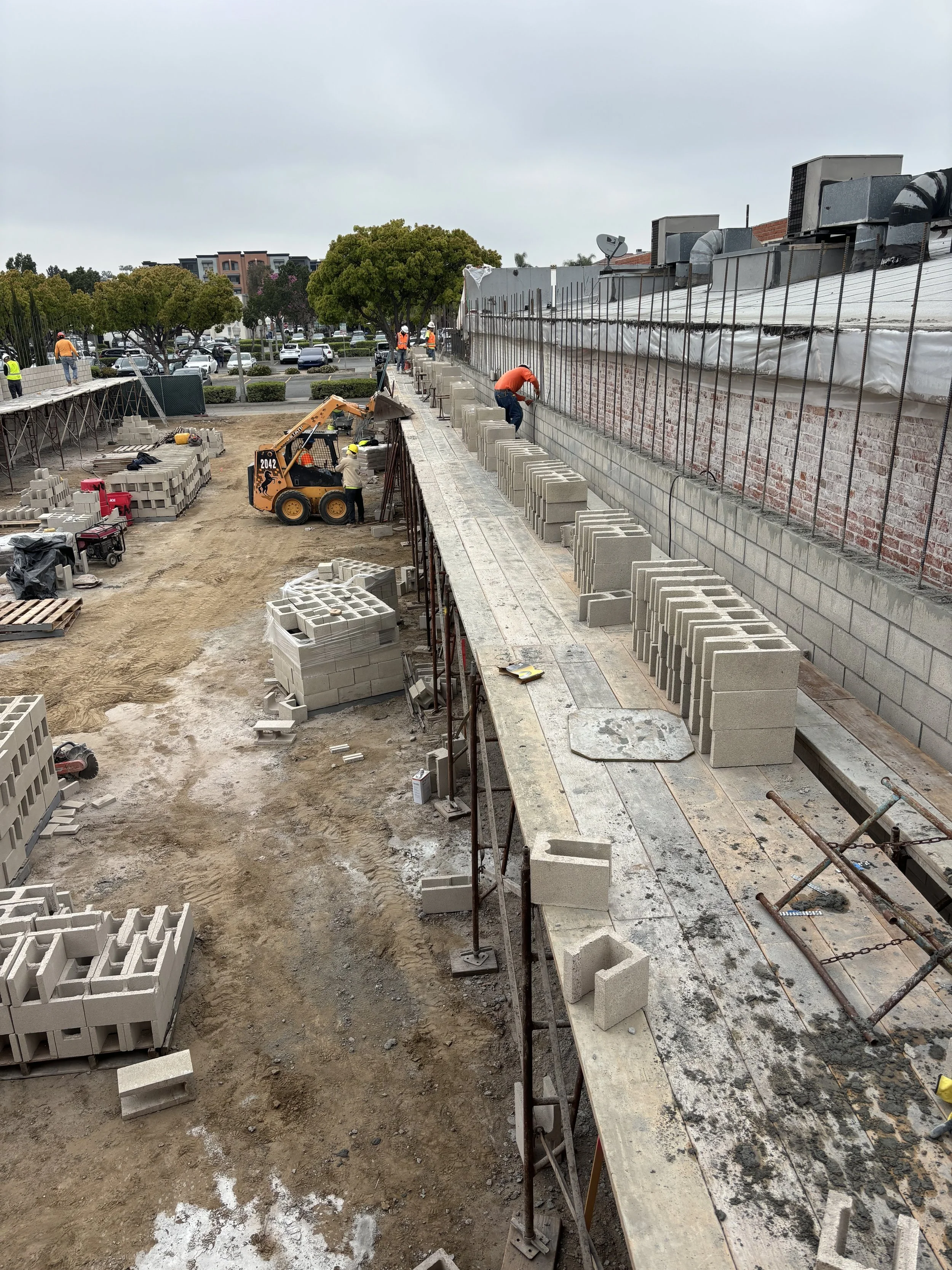 Construction workers building a brick wall on an outdoor construction site with cinder blocks and machinery.
