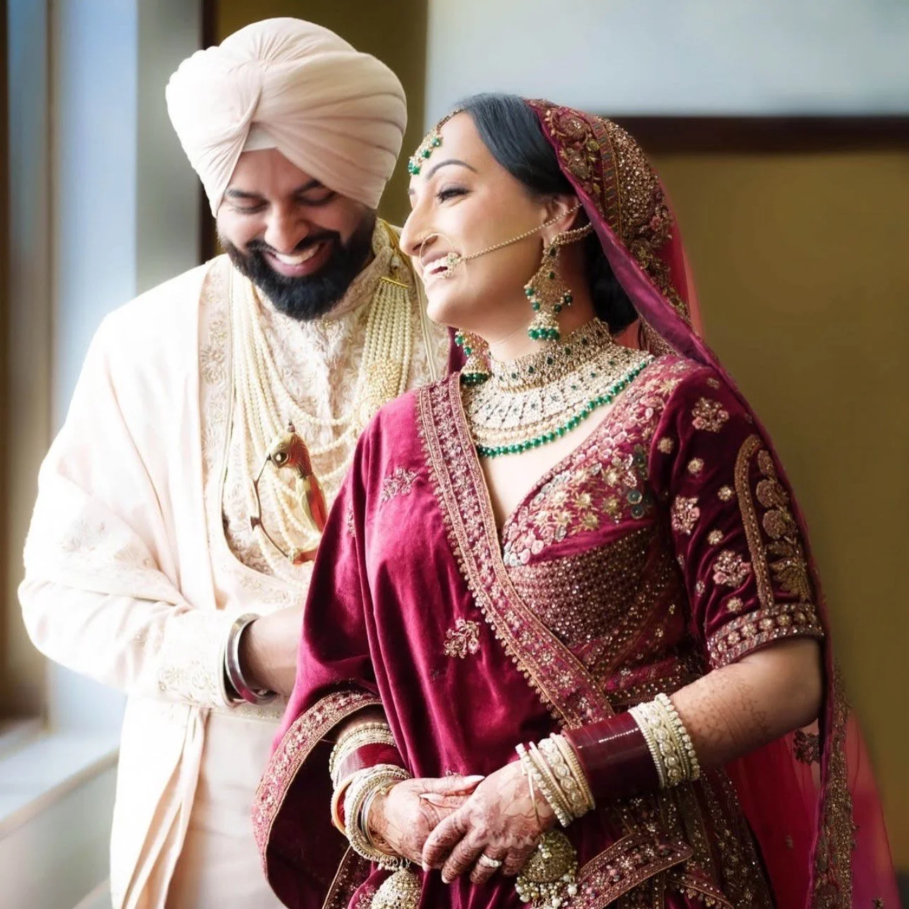 A couple dressed in traditional Indian wedding attire, smiling and sharing a joyful moment.