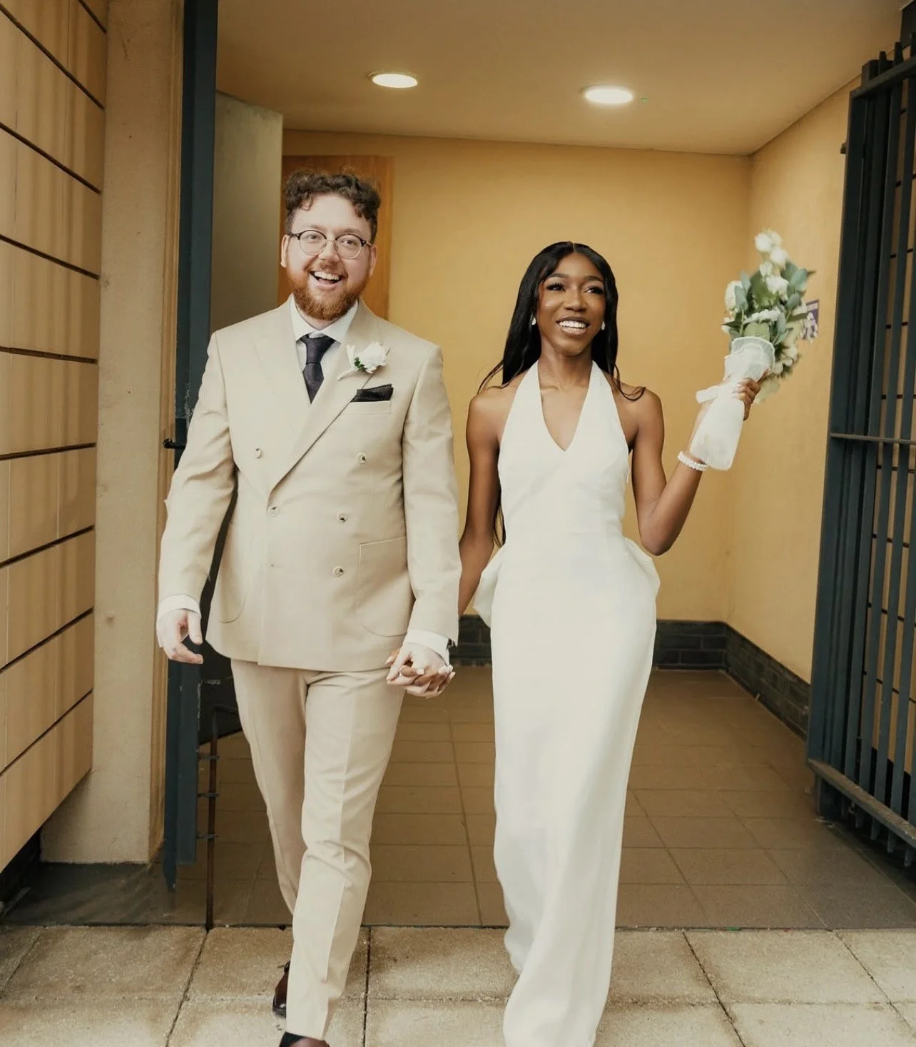 A couple in wedding attire holding hands and walking together, smiling and happy.