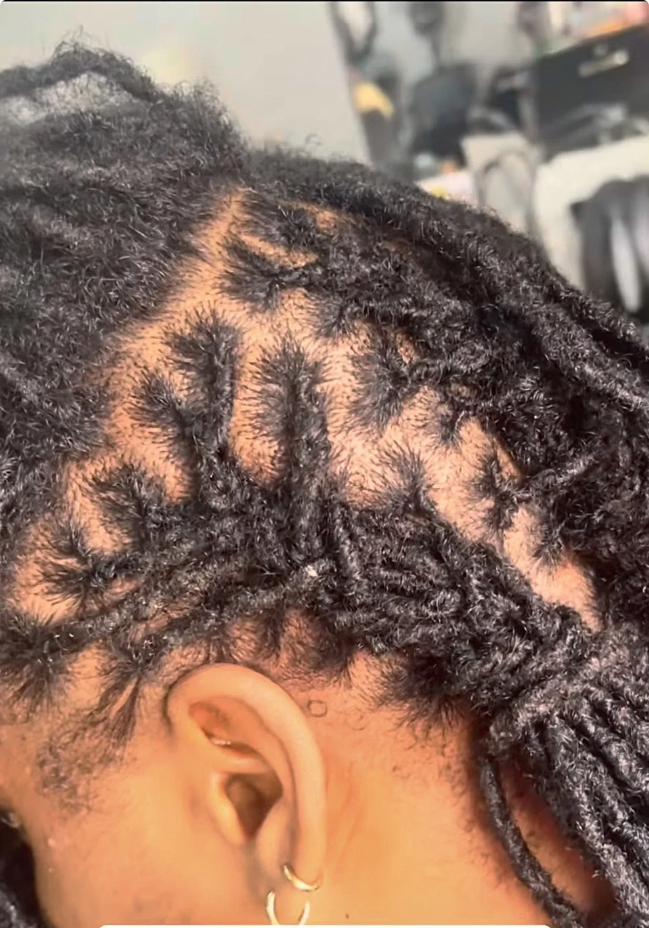Close-up of a person's head showing freshly styled dreadlocks with a neat fade on the sides, earrings in the ear, and part of the ear visible.