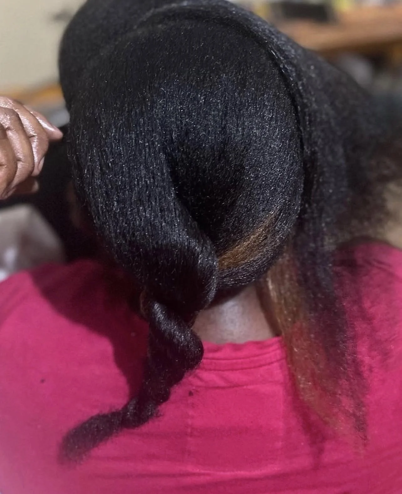 Close-up of a person's head with freshly styled long black hair, wrapped around the scalp, with a small curl at the end, wearing a pink shirt.