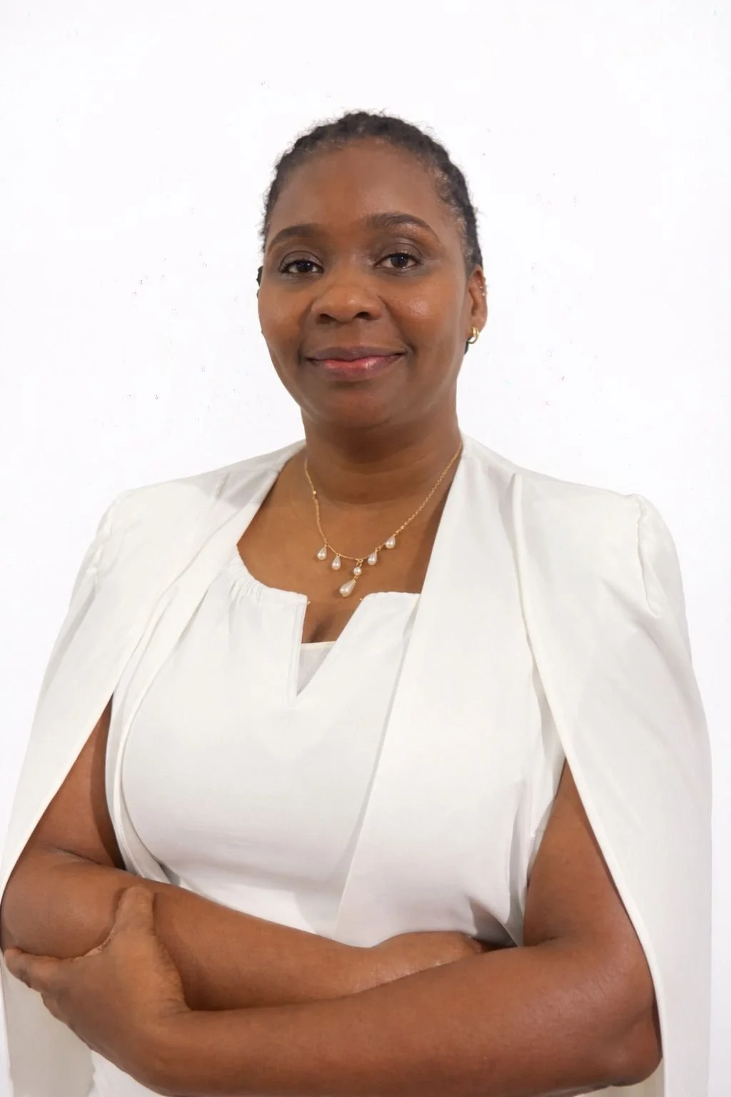 Portrait of a confident woman with crossed arms, wearing a white top, with jewelry, smiling softly, against a plain white background.