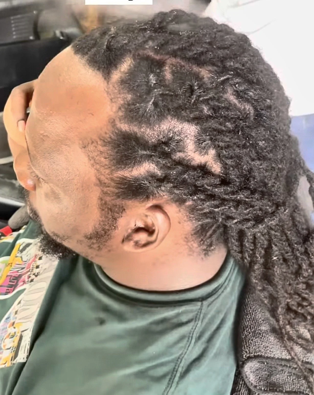 Side view of a person at a barbershop getting their hair styled into twists, with freshly cut sides and a fade haircut.