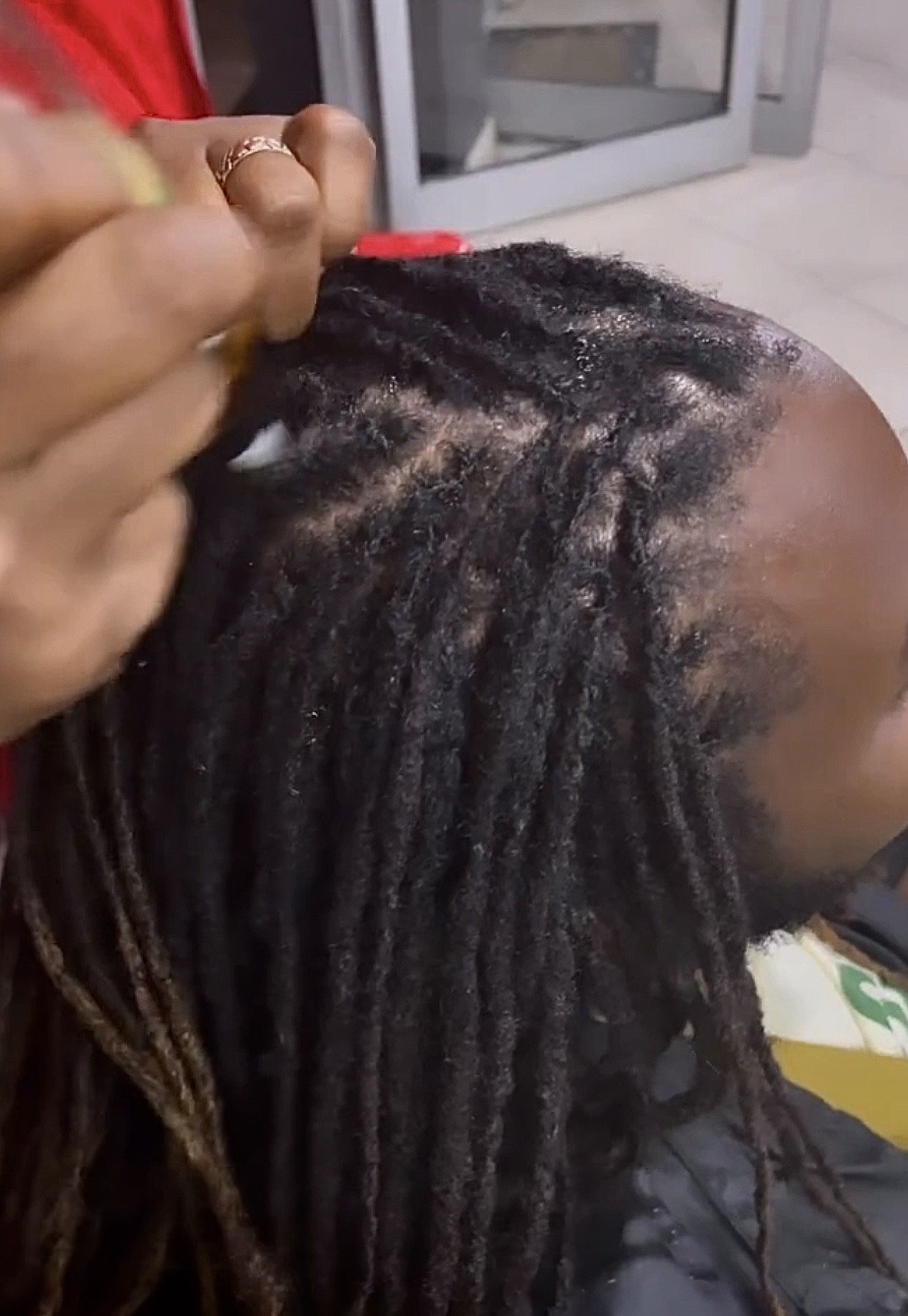 A person with long, thick dreadlocks combing or styling their hair in an indoor setting.