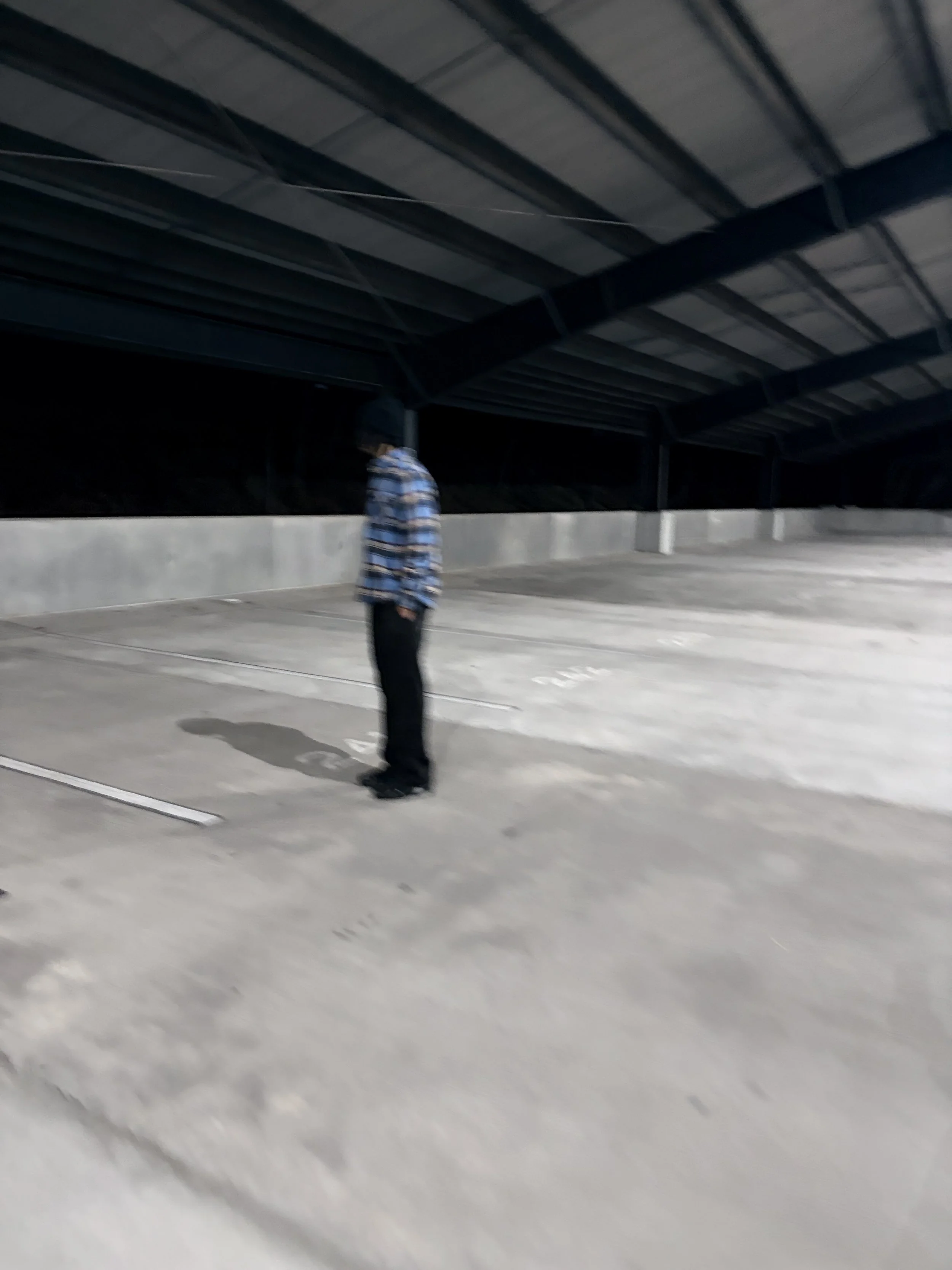 A person standing alone in an empty, dimly lit parking garage at night, wearing a striped hoodie and dark pants.