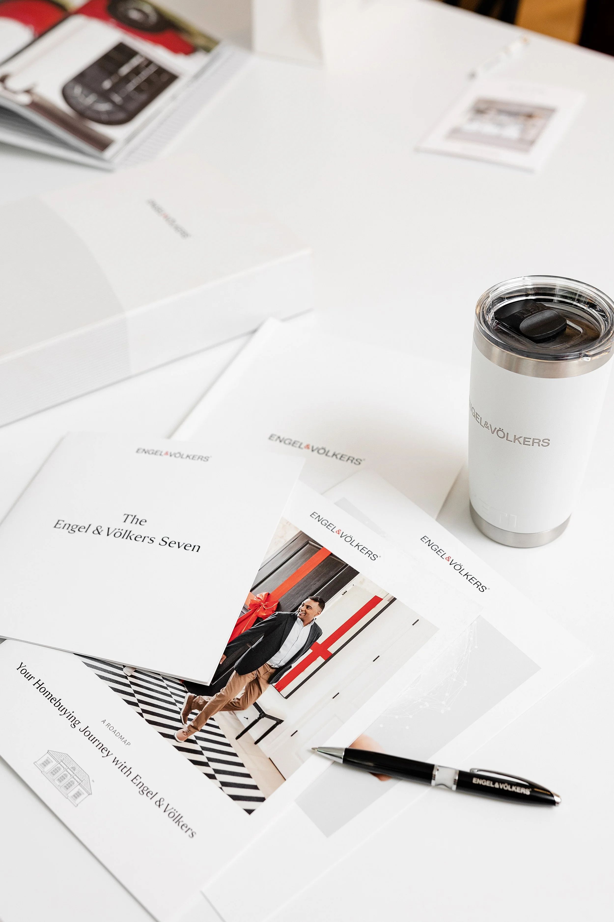 Business meeting materials on a white table, including brochures, a pen, and a travel mug with the Engel & Völkers logo.