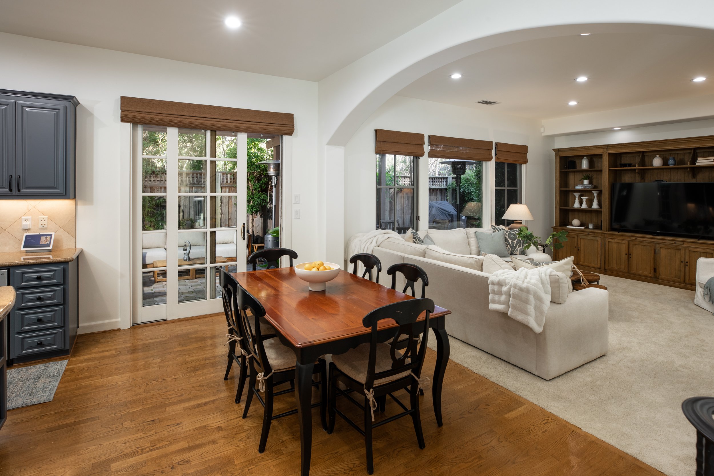 Bright living room with white sofa, wooden TV cabinet, and large windows showing outdoor patio.