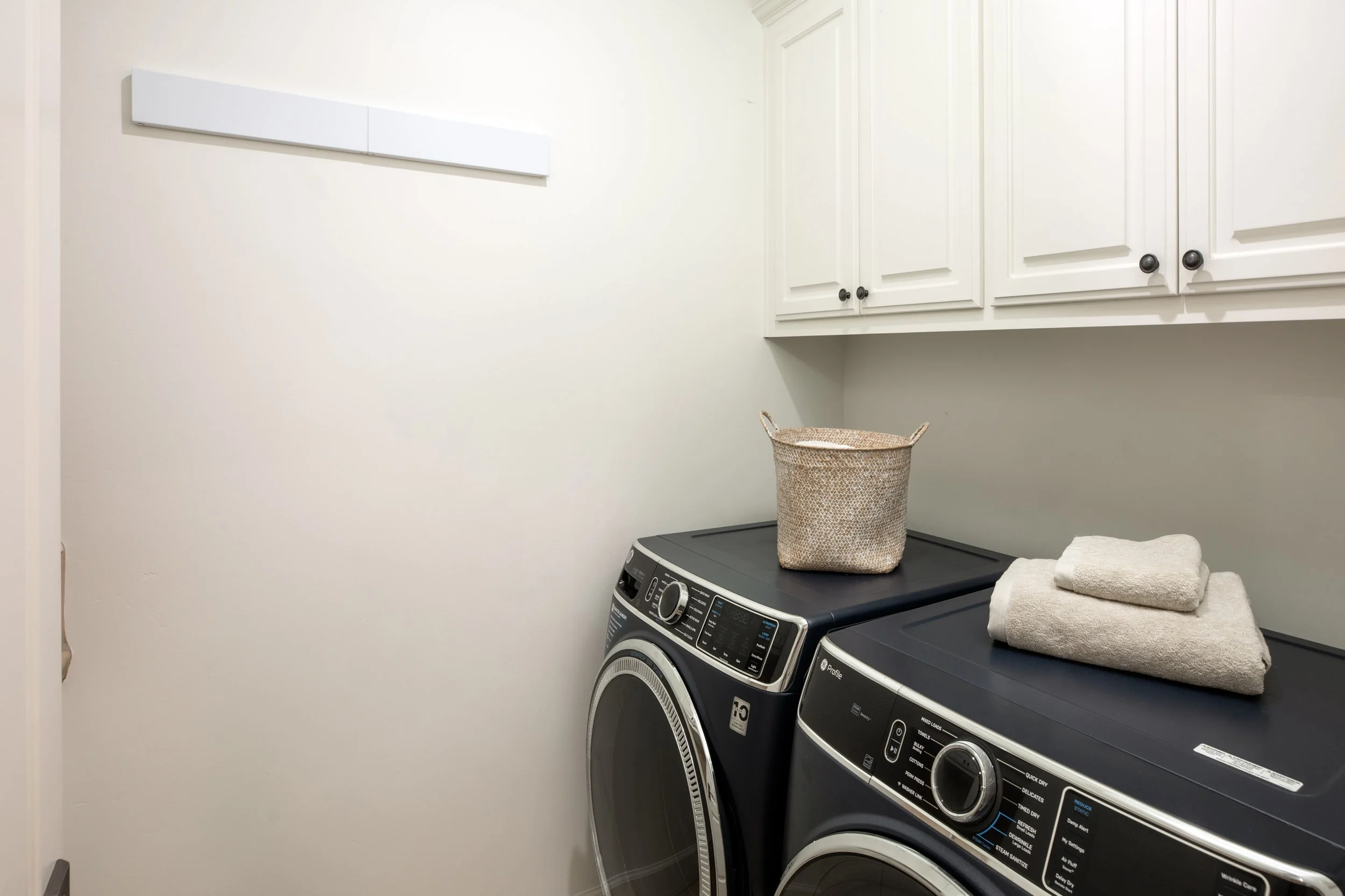 Laundry room with white cabinets, a washer and dryer, a basket, and folded towels.
