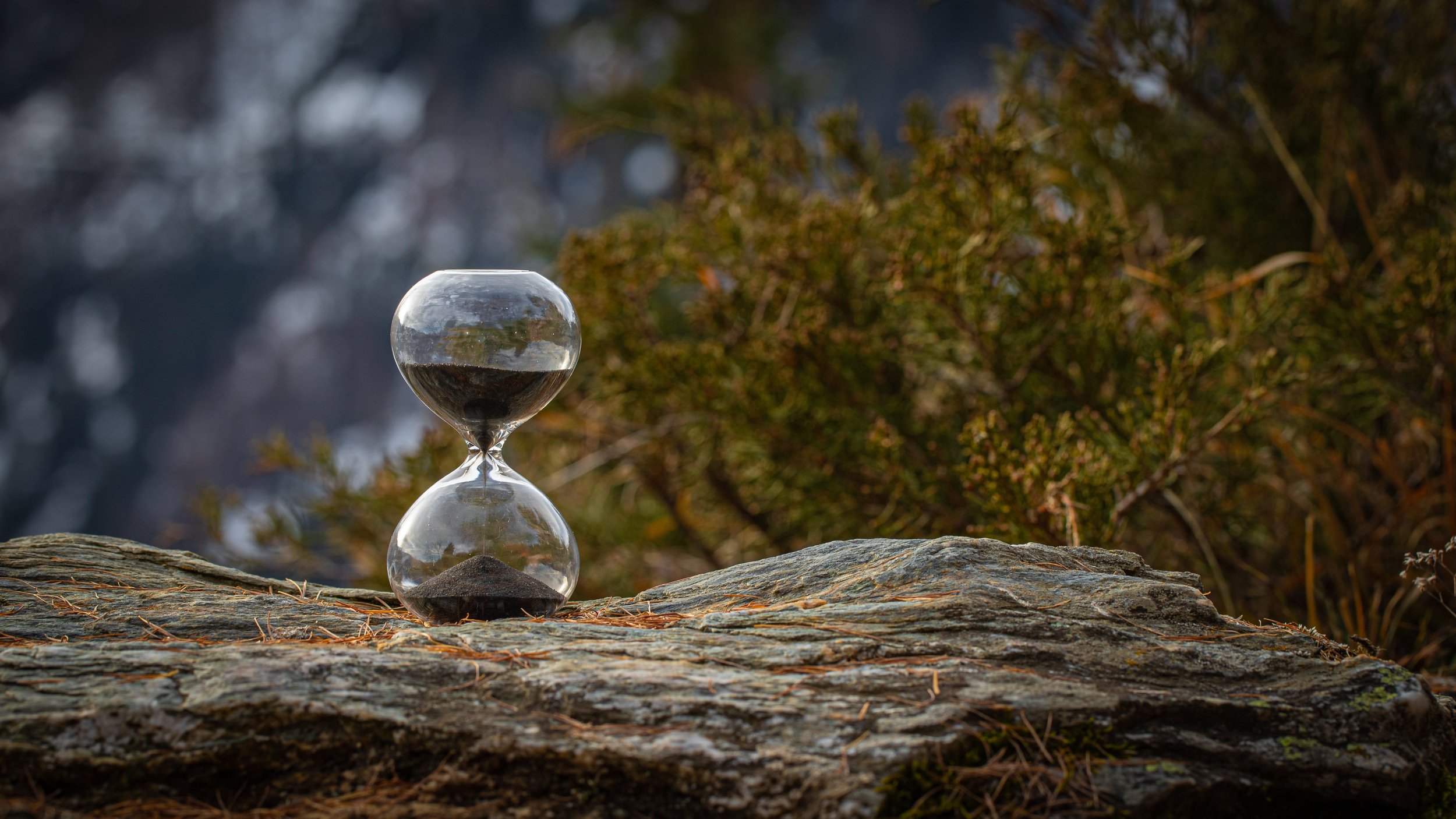 Glass hourglass resting on a rock outdoors, representing time and the long process of living with food intolerances