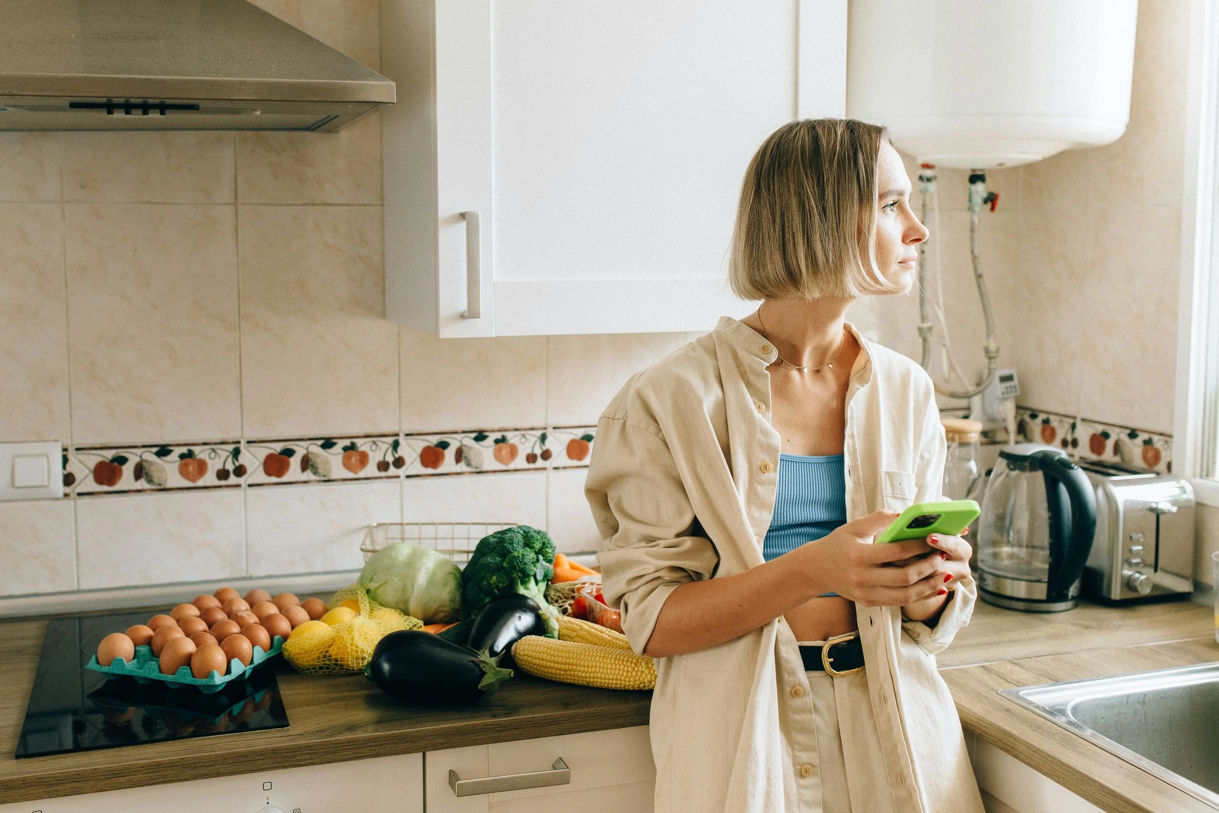 Woman standing in kitchen with fresh vegetables looking thoughtful representing the early stage of managing food sensitivities