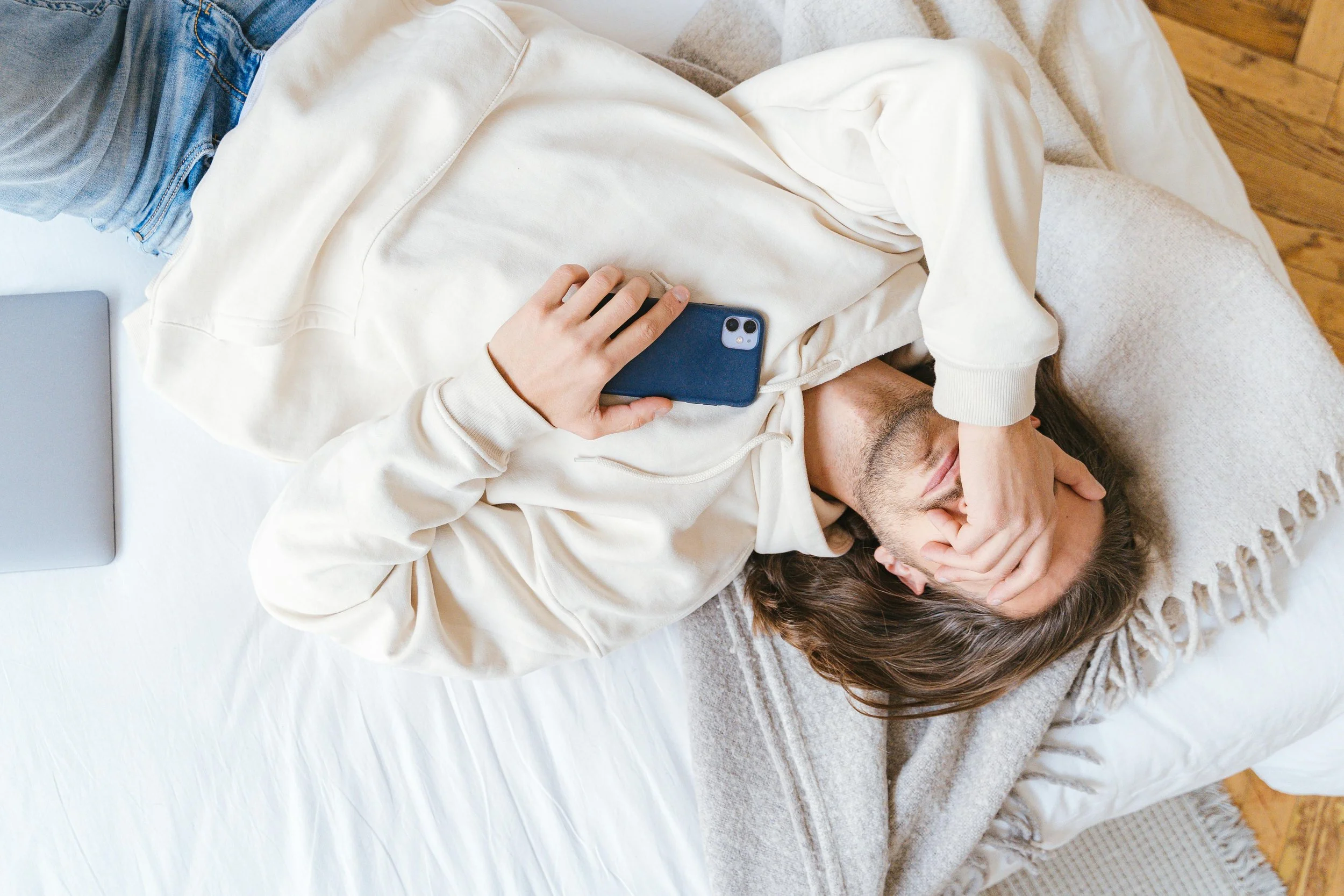 Man lieing on bed covering his eyes and holding a phone