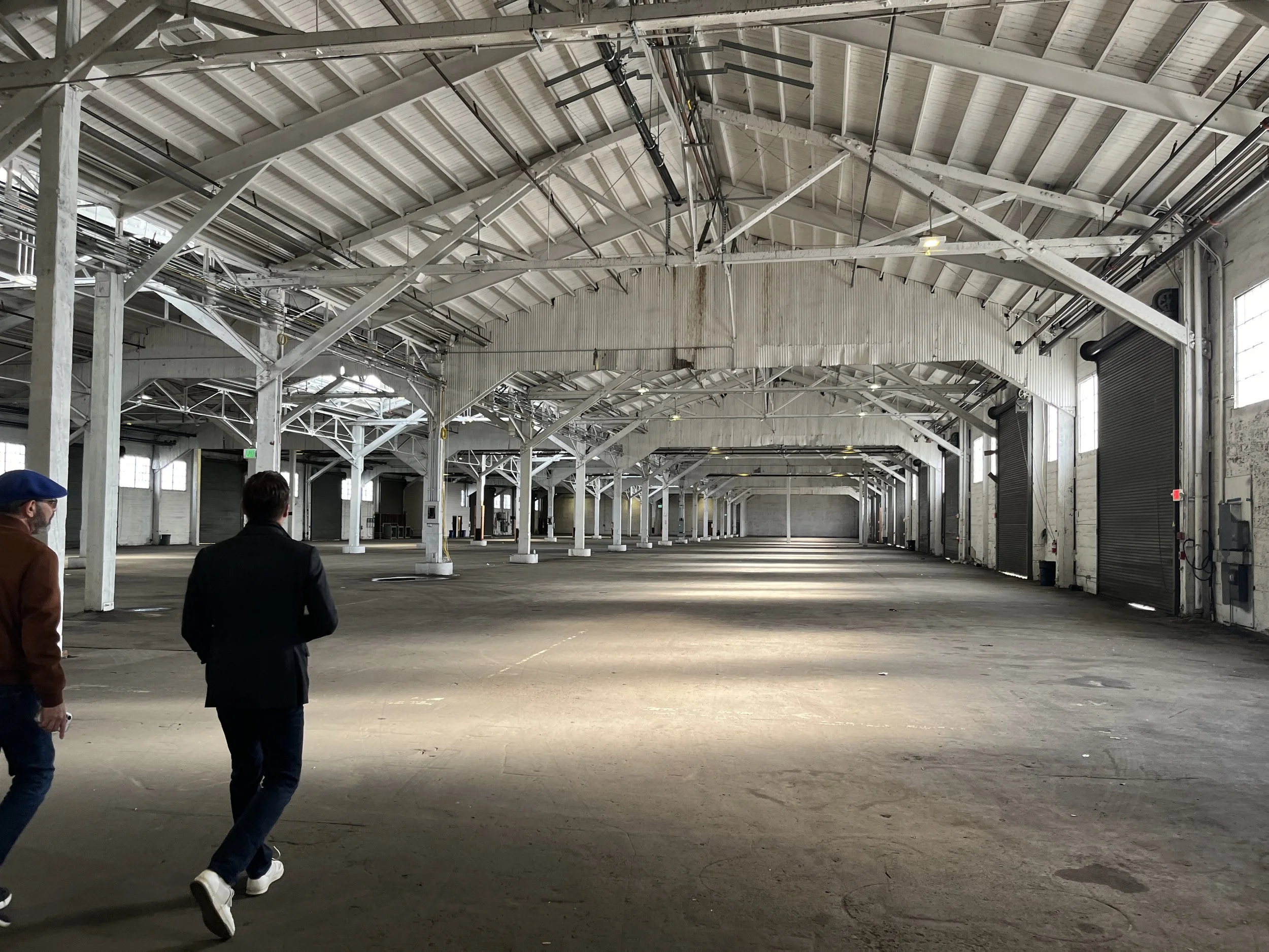 CAST staff tour of Pier 29 warehouse space showing expansive industrial interior with exposed beams and white columns