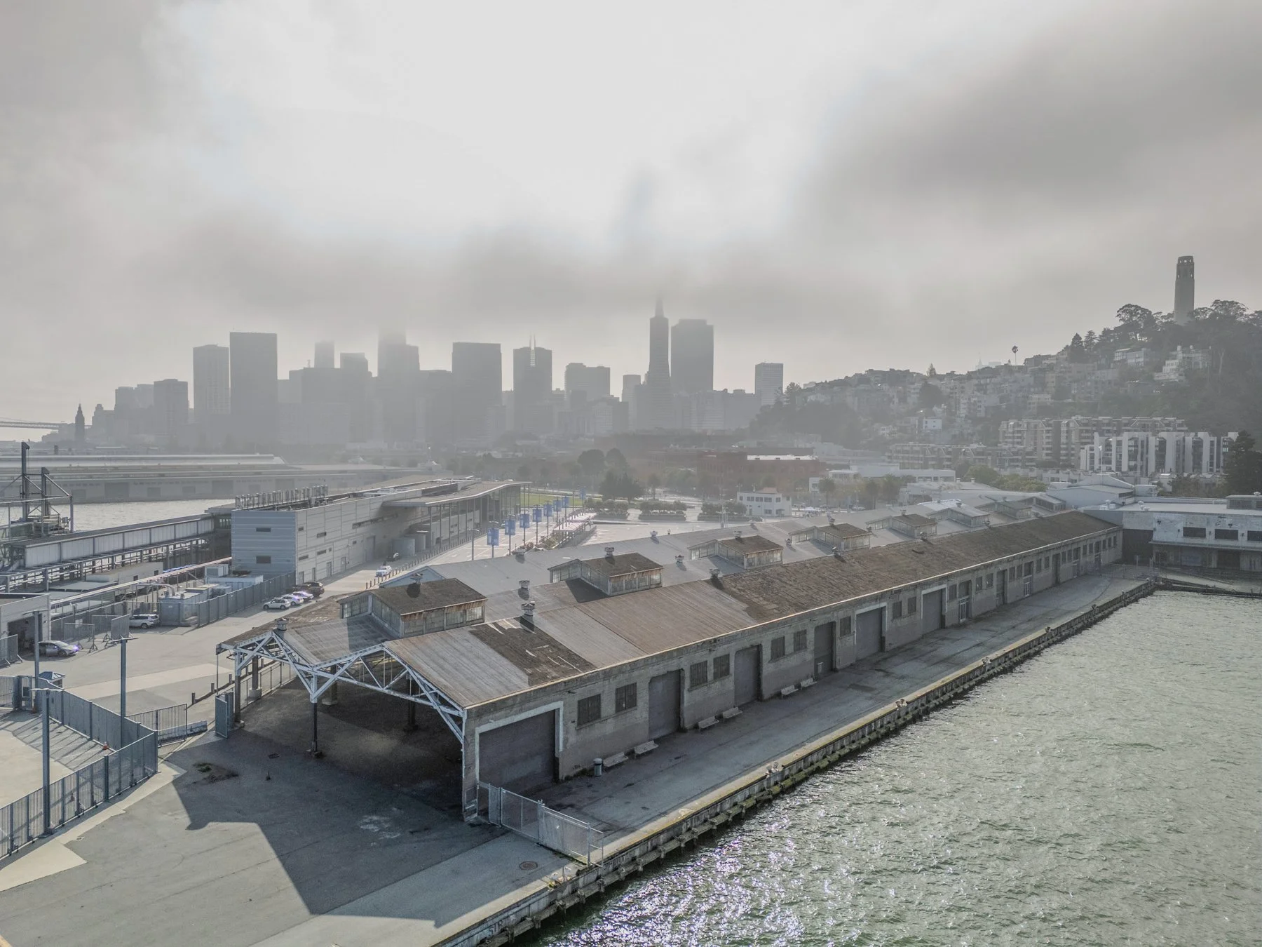 Drone shot of historic Pier 29 waterfront warehouse on Embarcadero overlooking San Francisco downtown skyline with Coit Tower on Telegraph Hill