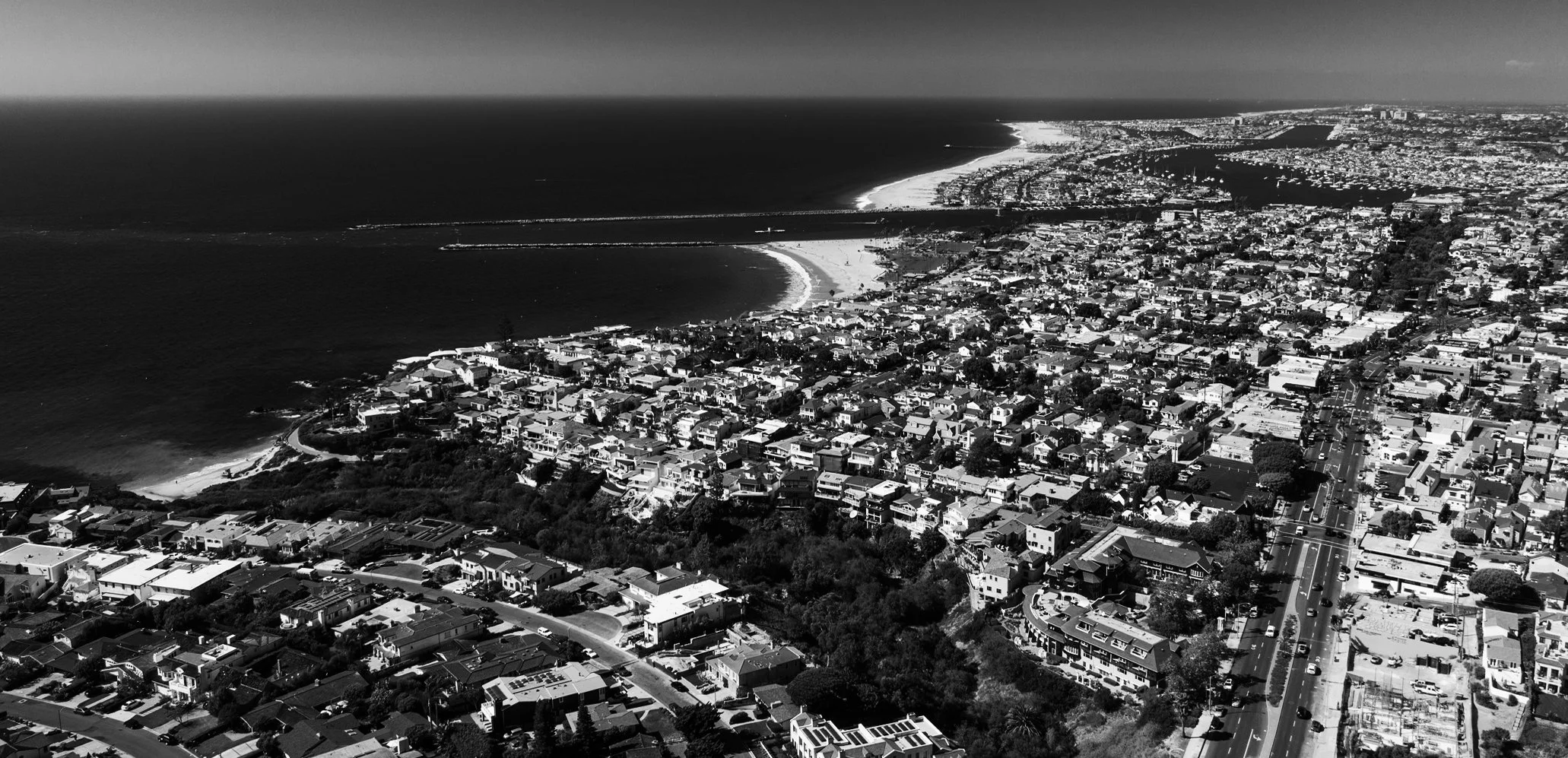 Aerial view of a coastal city with a beach, residential area, and streets, in black and white.