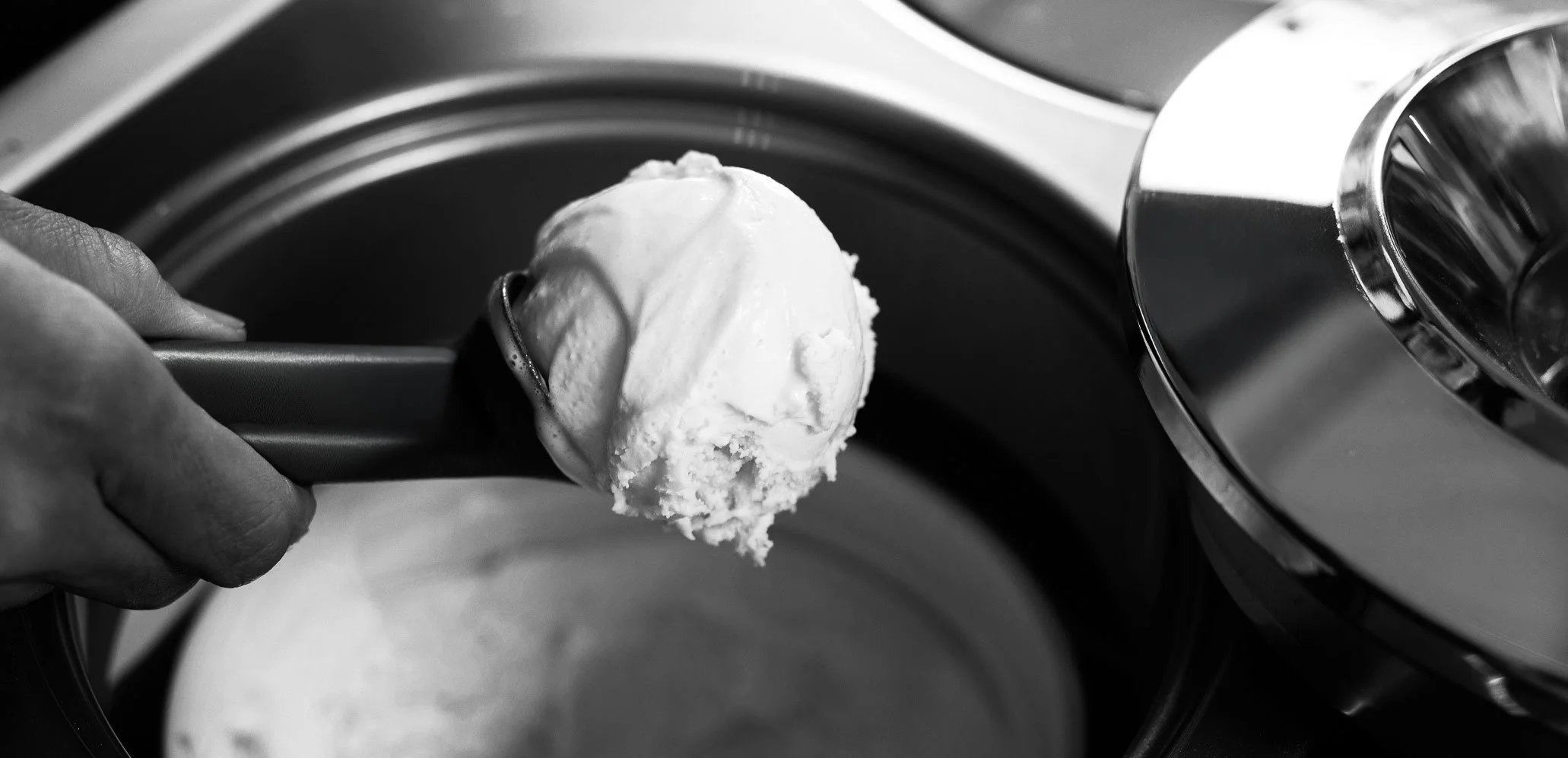 Close-up of a hand holding a scoop of vanilla ice cream near a washing machine's door.