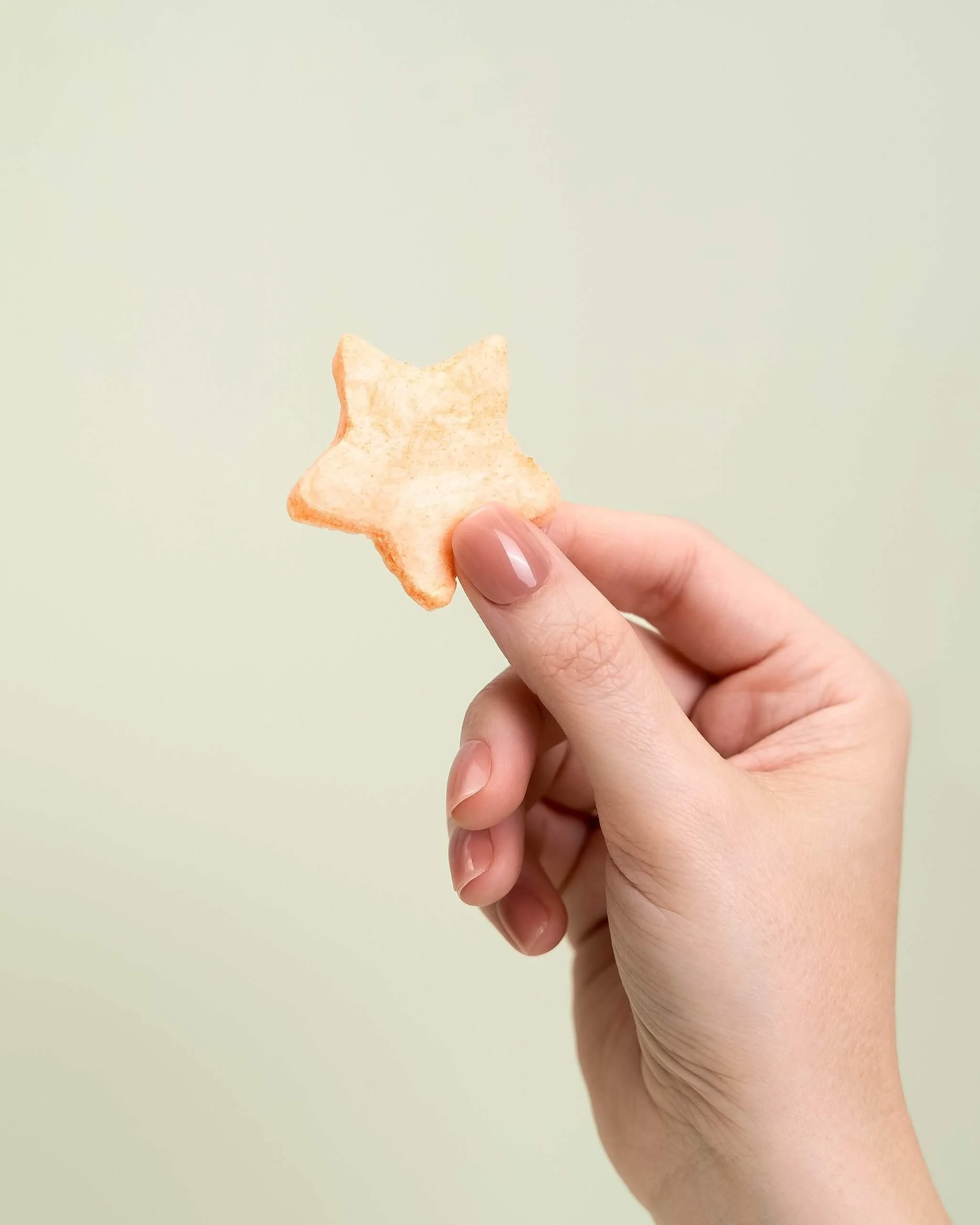 A hand holds a orange cotton candy star in front of an olive green background