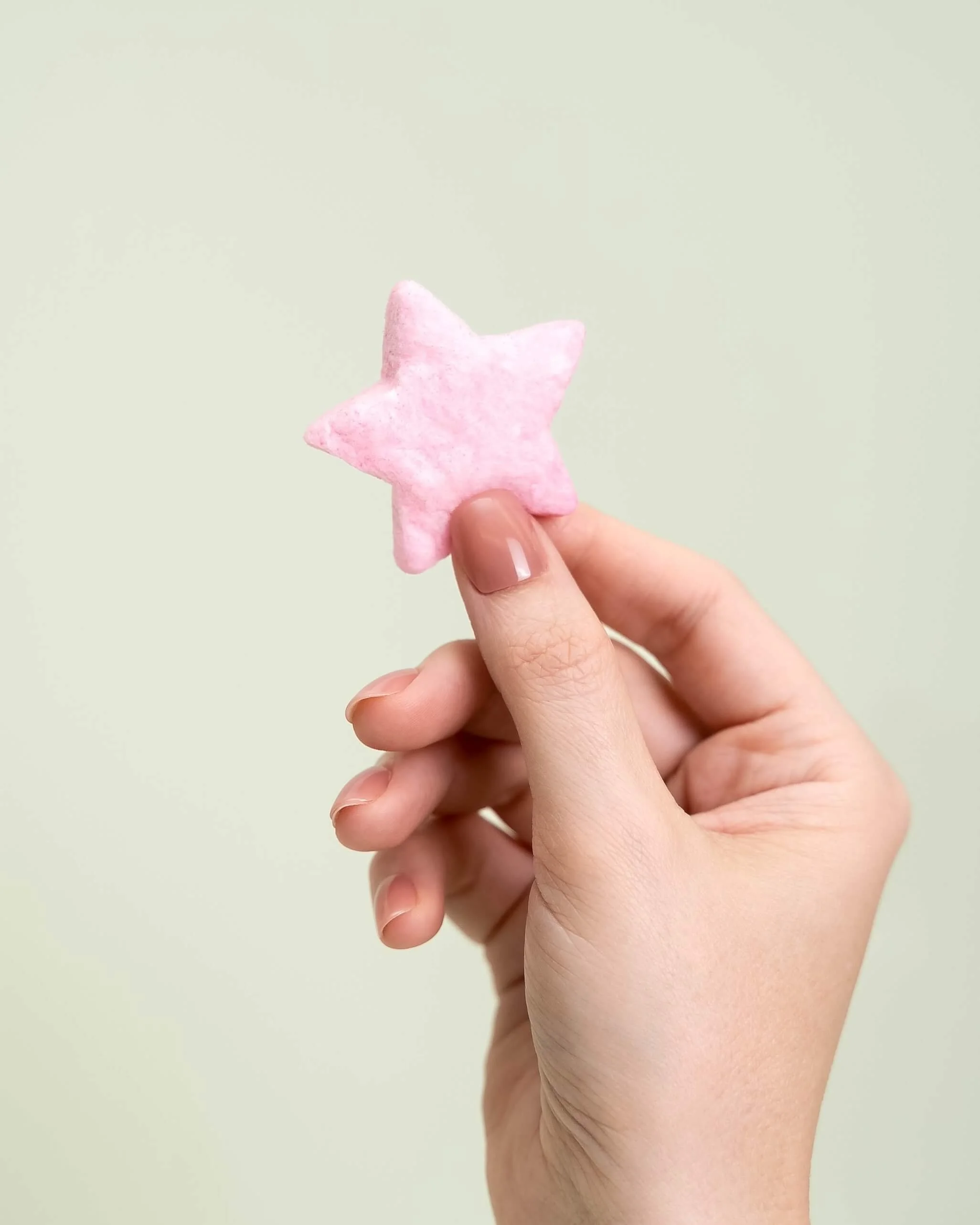 A hand holds a pink cotton candy star in front of an olive green background