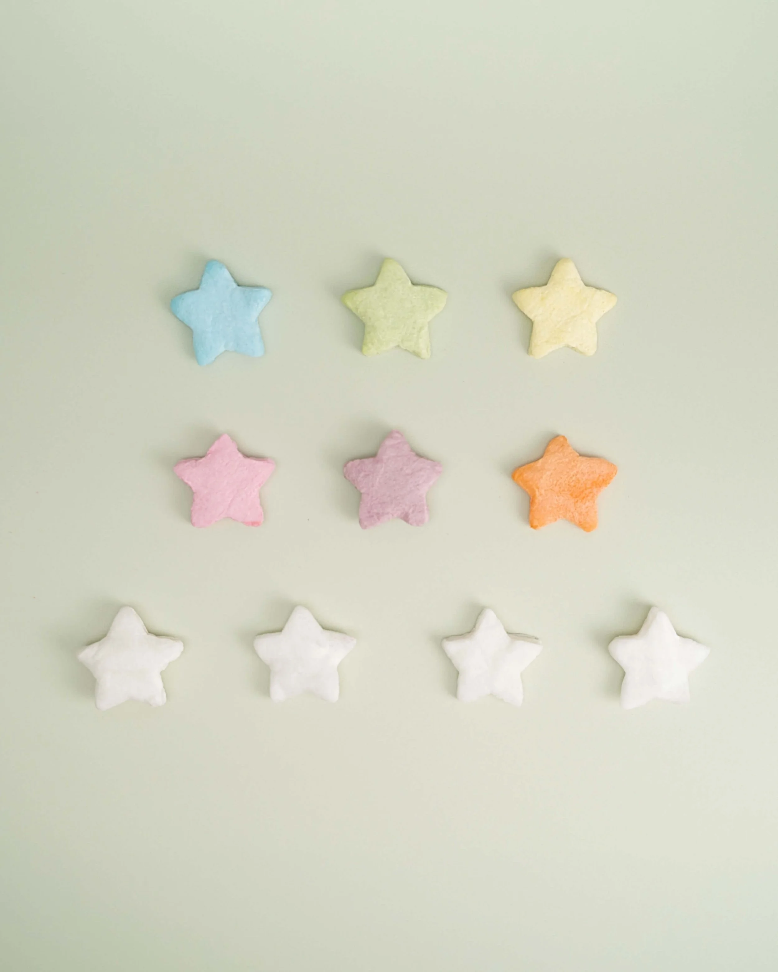 Colorful star-shaped cotton candy pieces arranged in rows on a light green background.