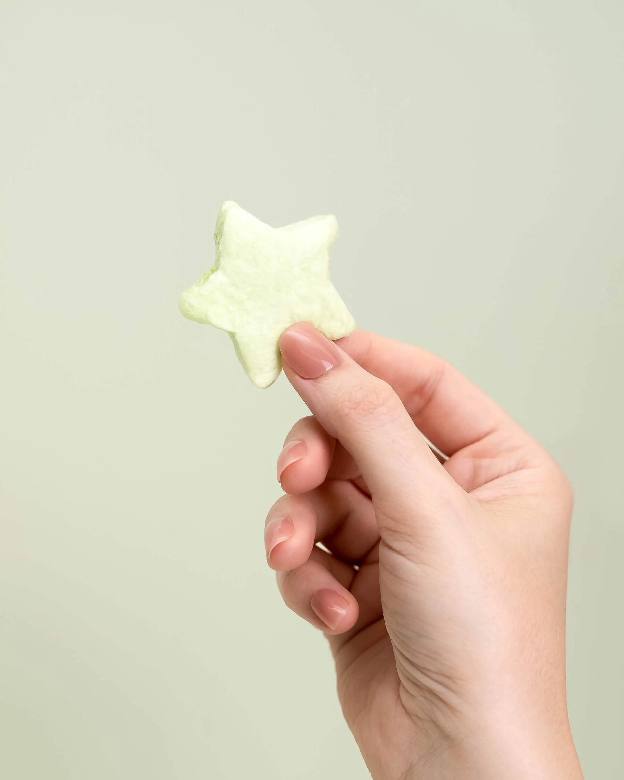 A hand holds a green cotton candy star in front of an olive green background