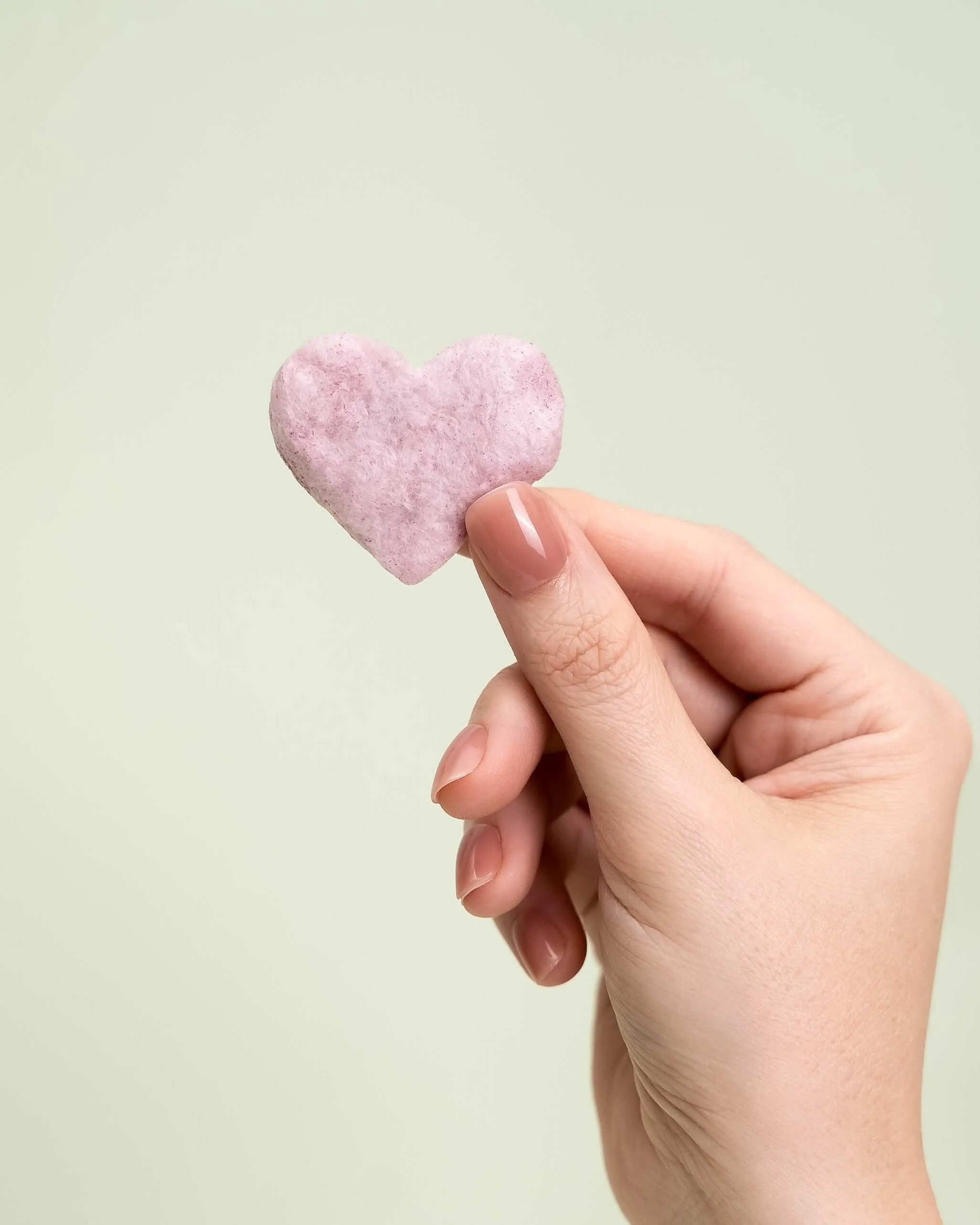 A hand holds a purple cotton candy heart in front of an olive green background