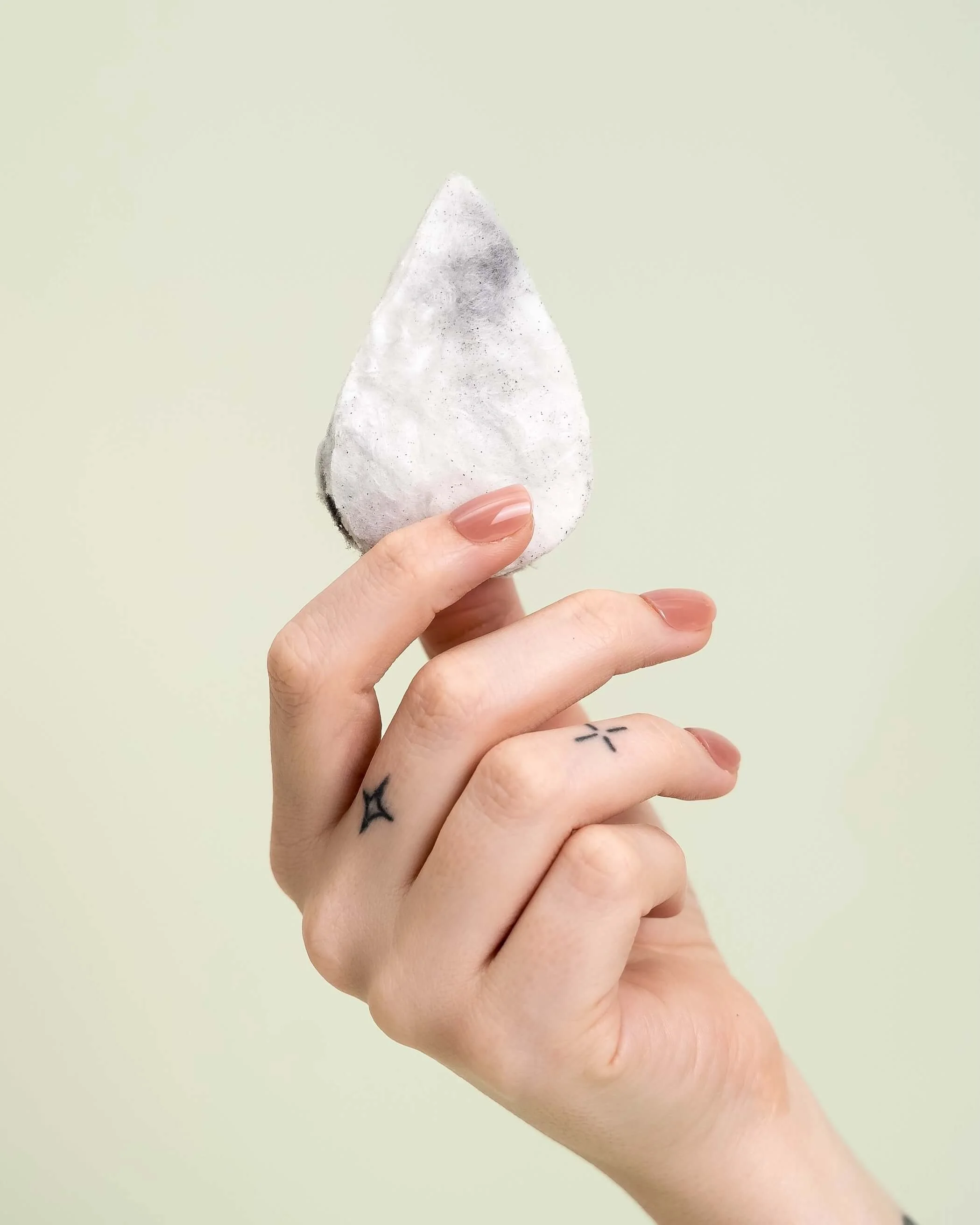 A hand holding a cotton candy drink drop against an olive green background