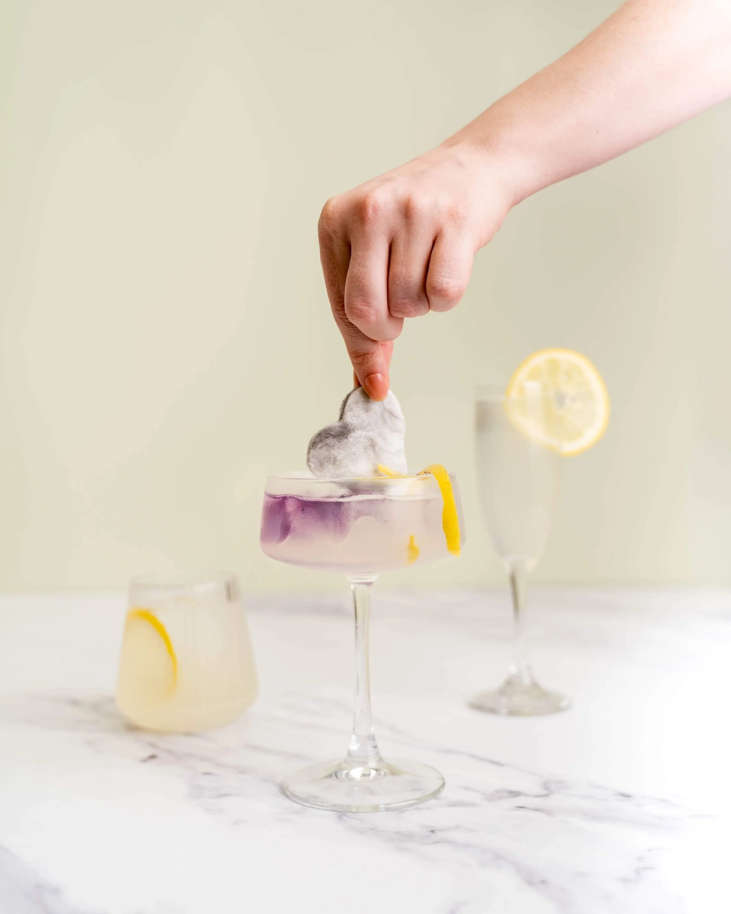 A hand dips drink drop cotton candy into a cocktail glass full of lemonade