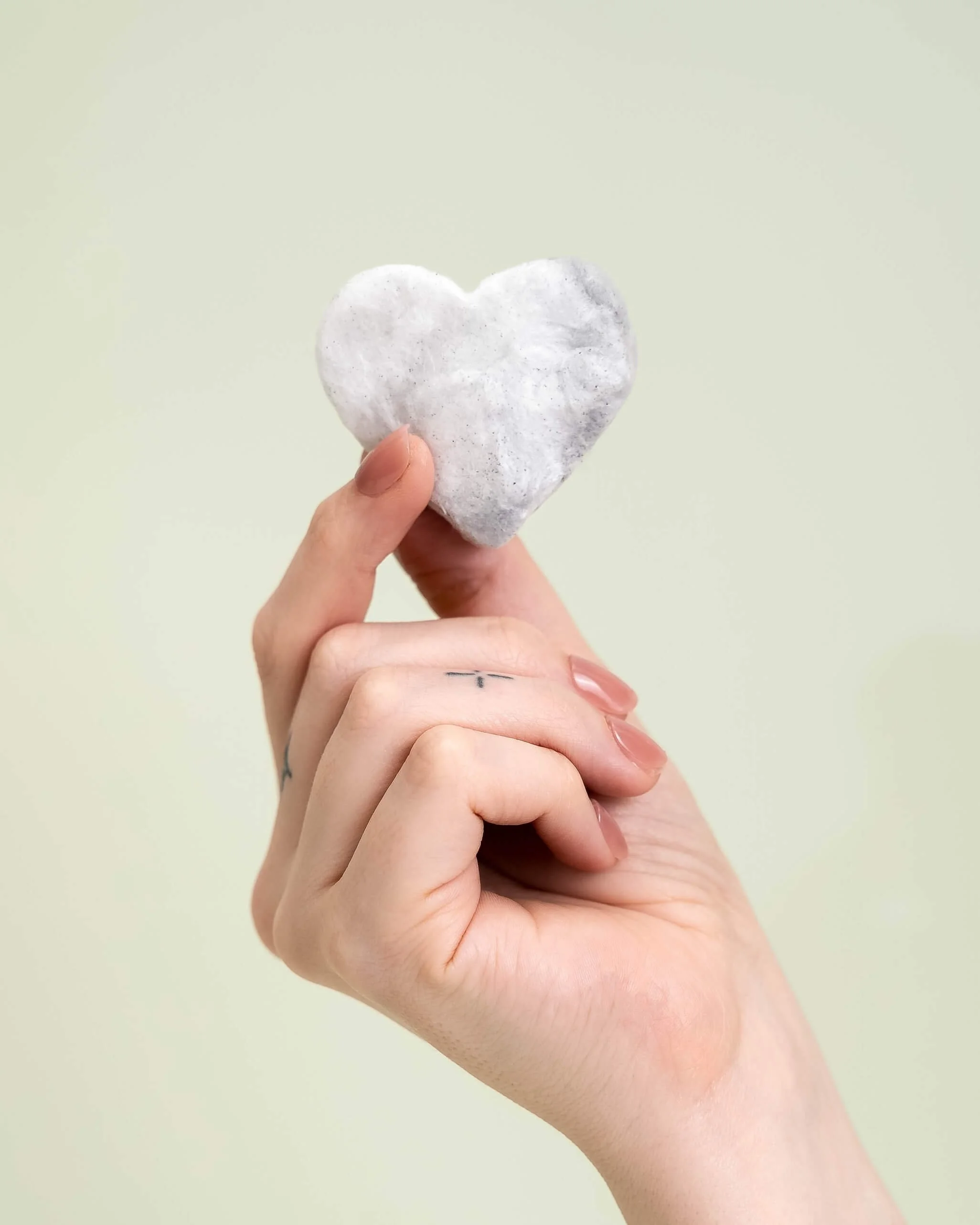 A hand holding a cotton candy drink drop against an olive green background