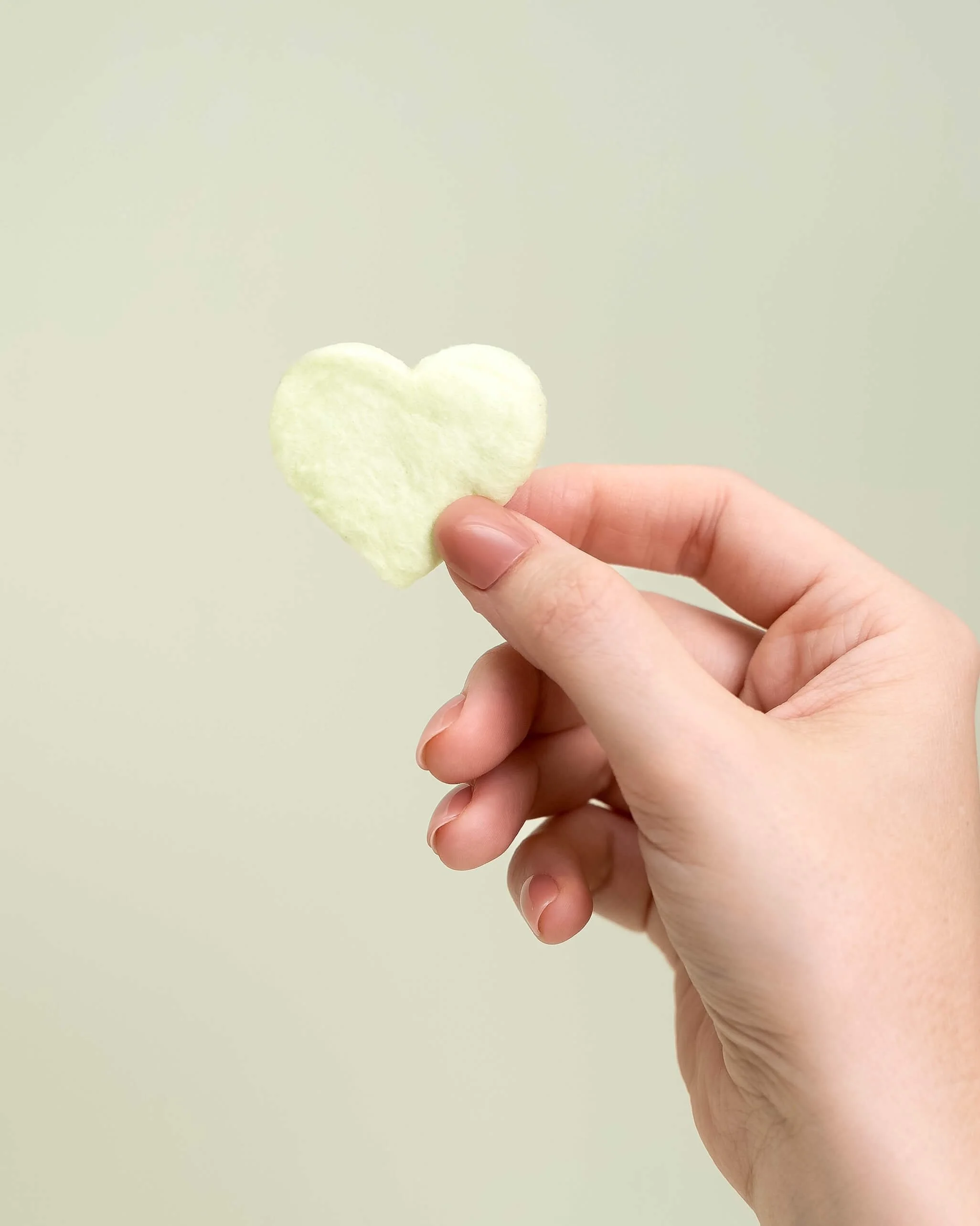 A hand holds a green cotton candy heart in front of an olive green background
