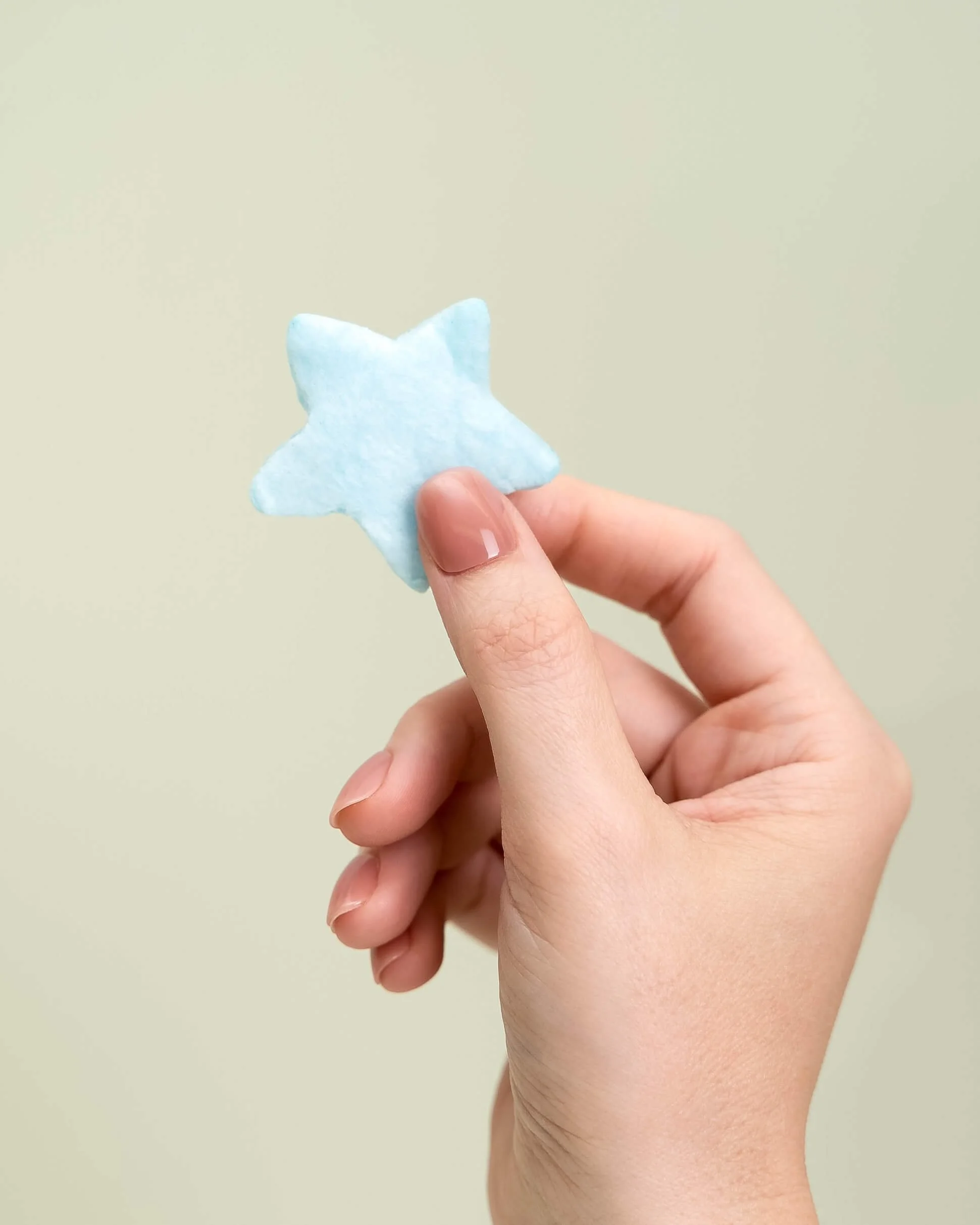A hand holds a blue cotton candy star in front of an olive green background