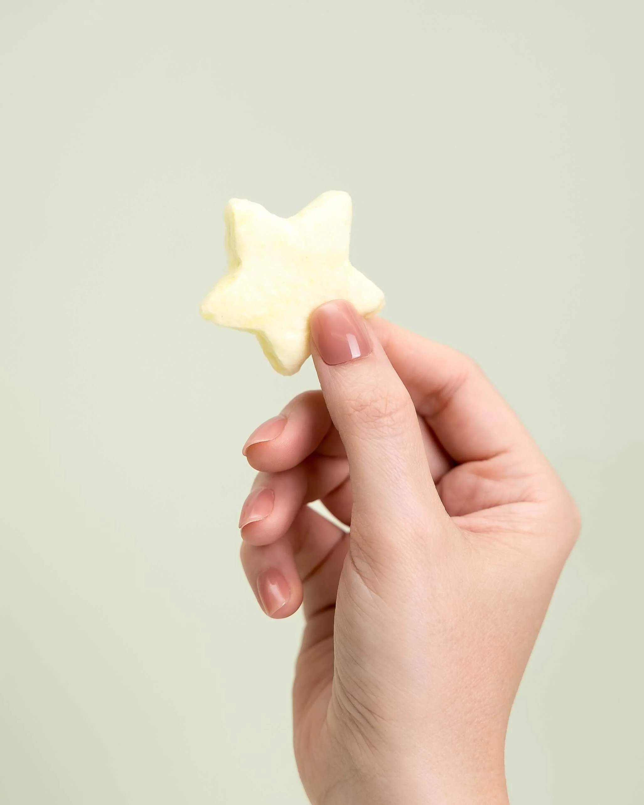 A hand holds a yellow cotton candy star in front of an olive green background