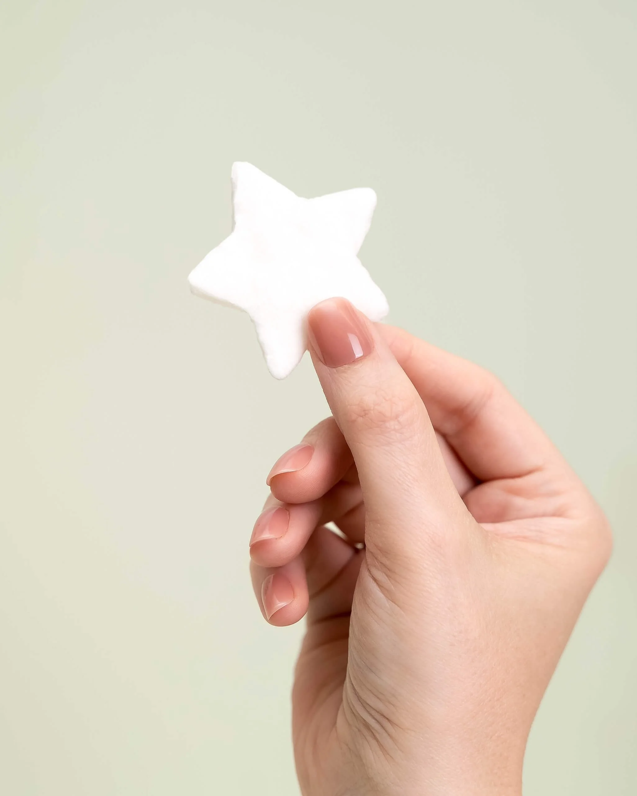 A hand holds a white cotton candy star in front of an olive green background