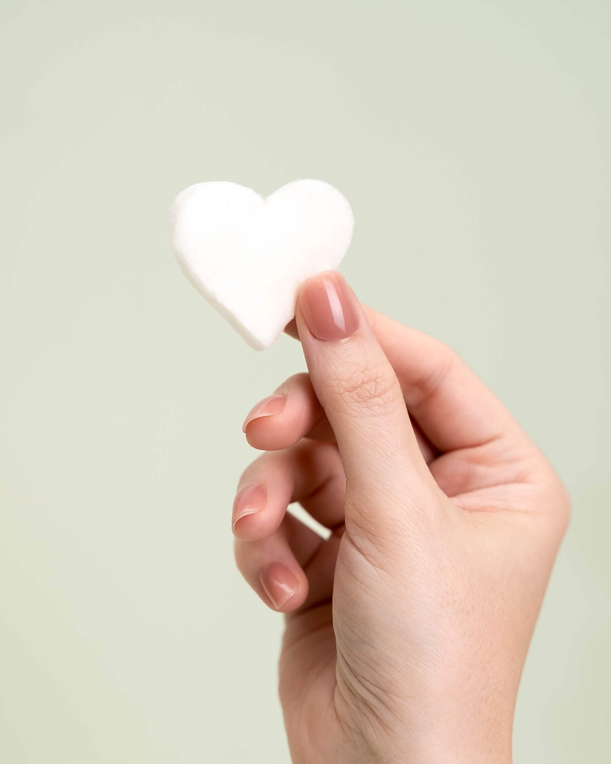 A hand holds a white cotton candy heart in front of an olive green background