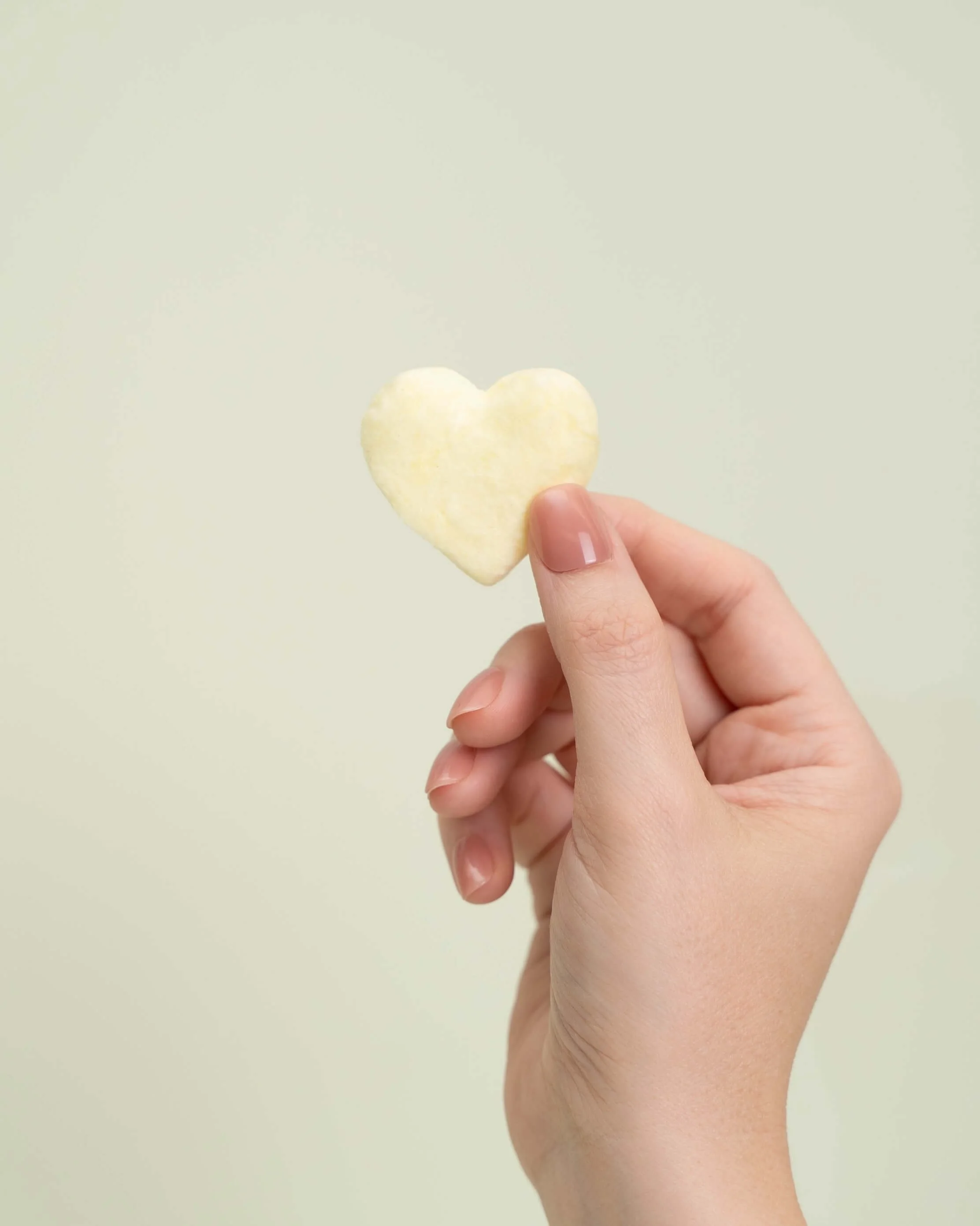 A hand holds a yellow cotton candy heart in front of an olive green background