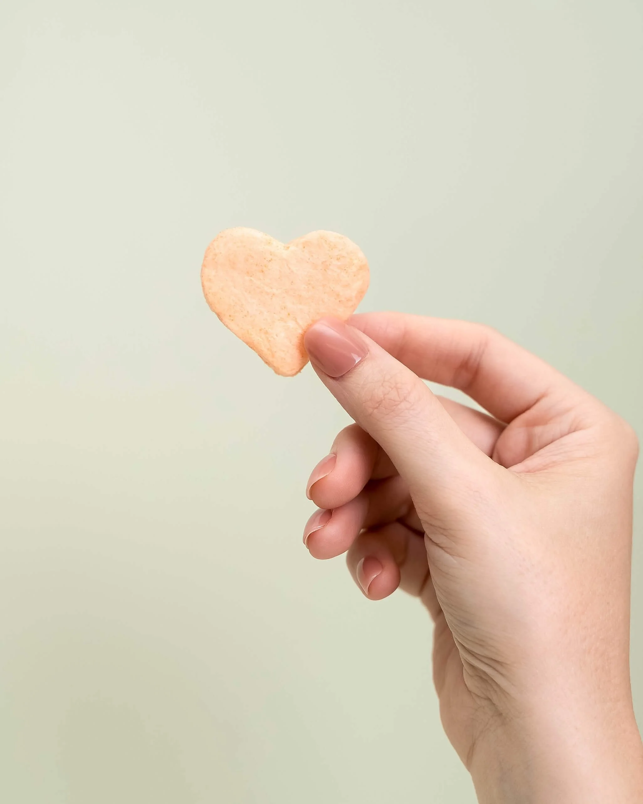 A hand holds a orange cotton candy heart in front of an olive green background