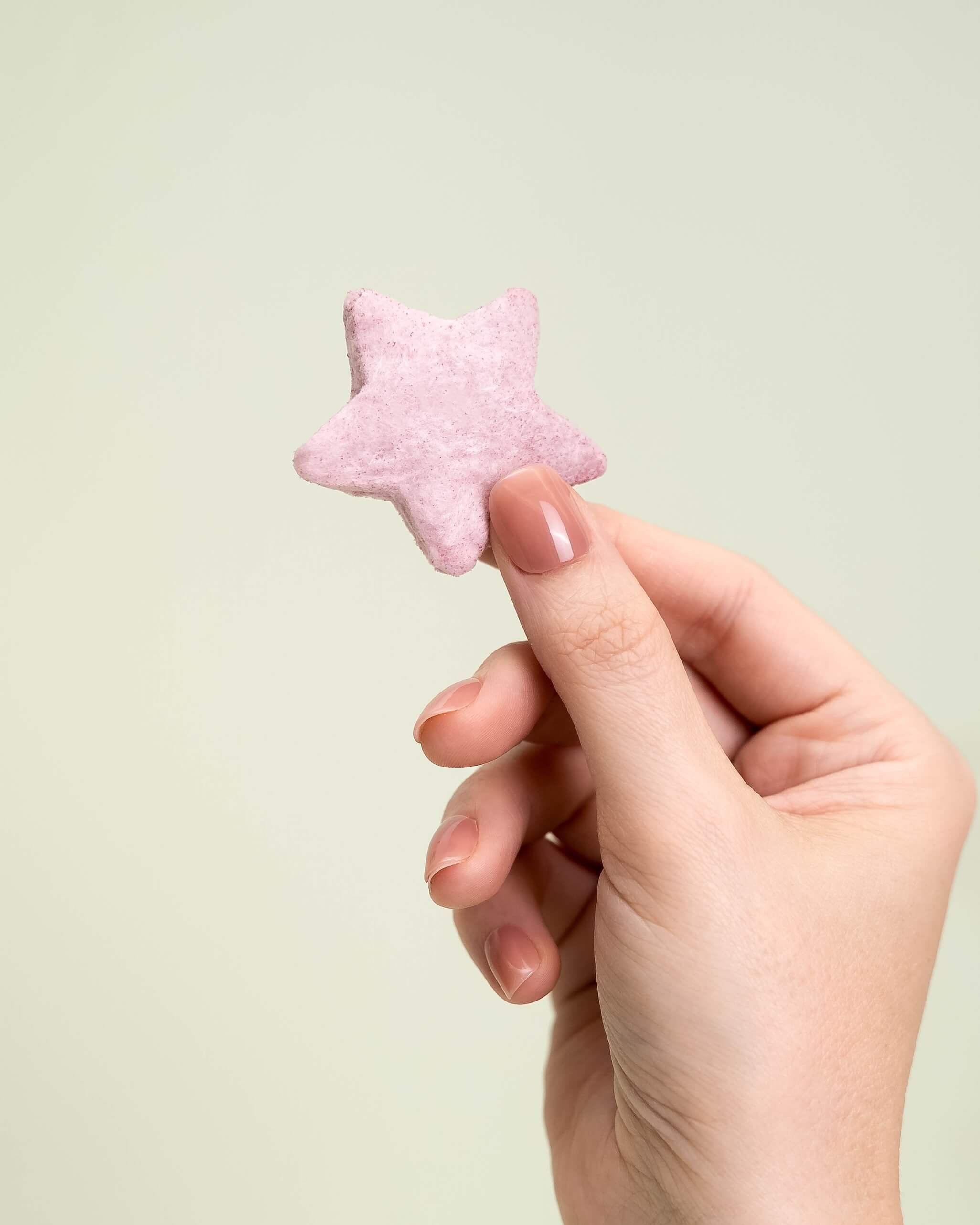 A hand holds a purple cotton candy star in front of an olive green background